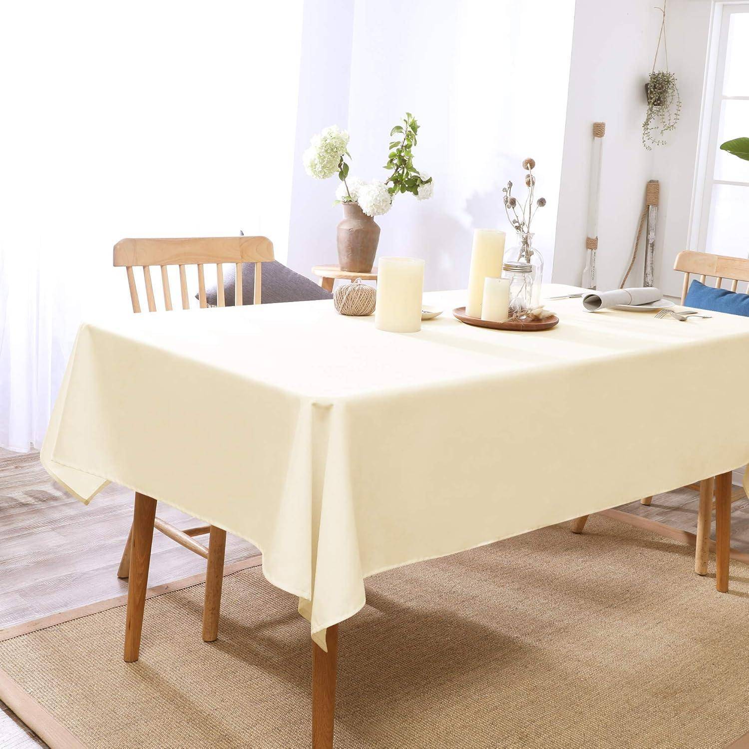 Ein Esszimmer mit einem Tisch, der mit einem beigen Tuch bedeckt ist, umgeben von Holzstühlen. Eine Vase mit Blumen und Kerzen steht auf dem Tisch.