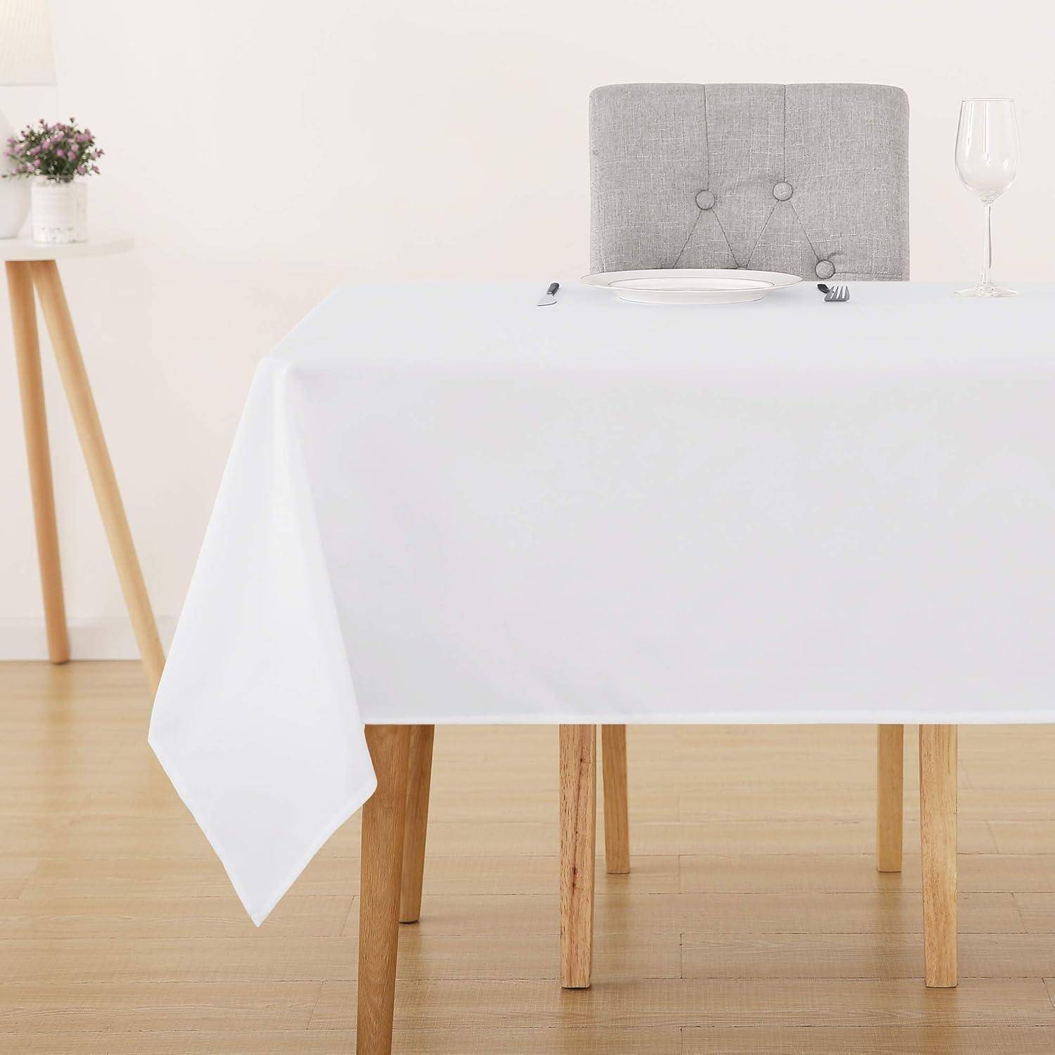 Eine Tischdekoration mit einem grauen gepolsterten Stuhl und einem Holztisch, der mit einem weißen Tischtuches bedeckt ist und mit einem Teller und einem Weinglas bestückt ist.