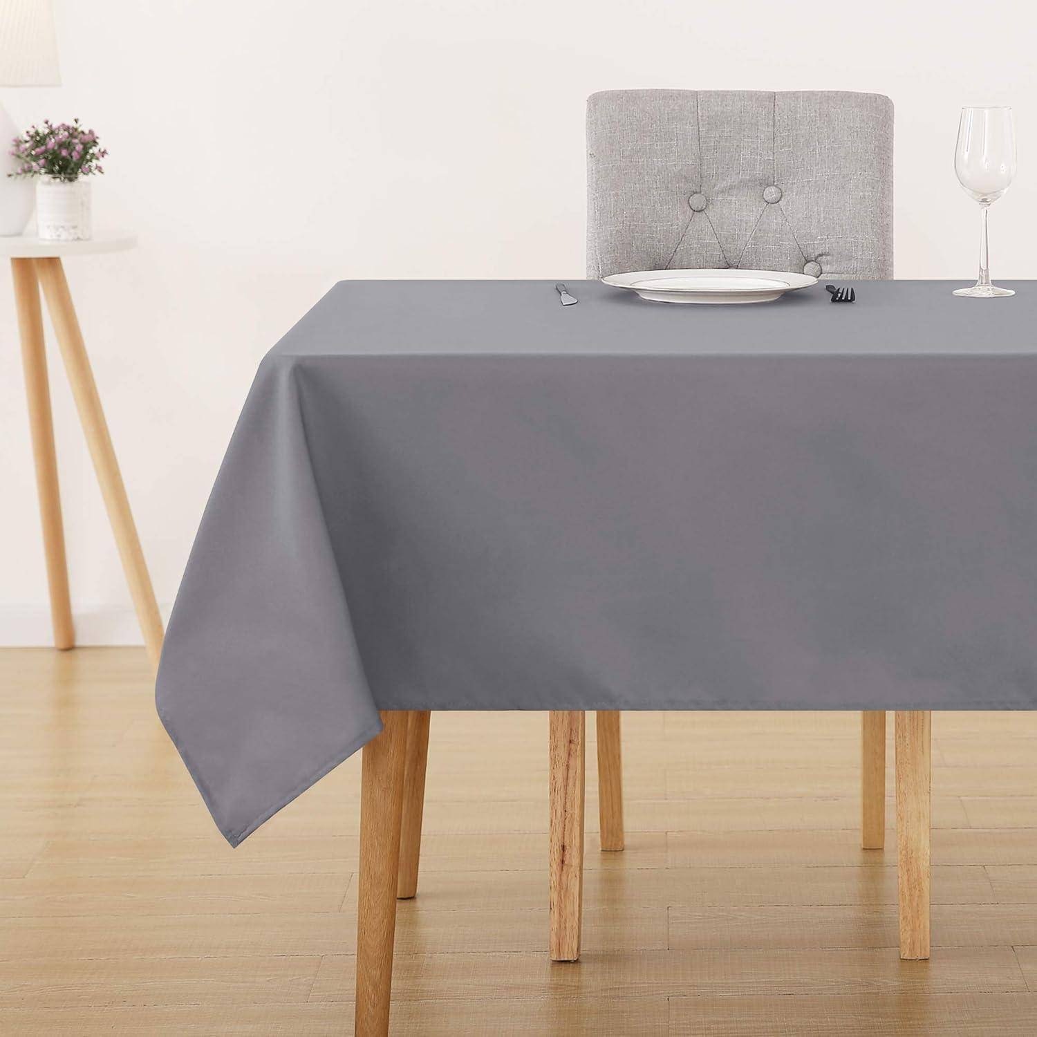 Ein Esstisch mit einer grauen Tischdecke, bestückt mit einem Teller, einer Gabel und einem Weinglas, steht in einem minimalistischen Raum mit hellem Holzboden.