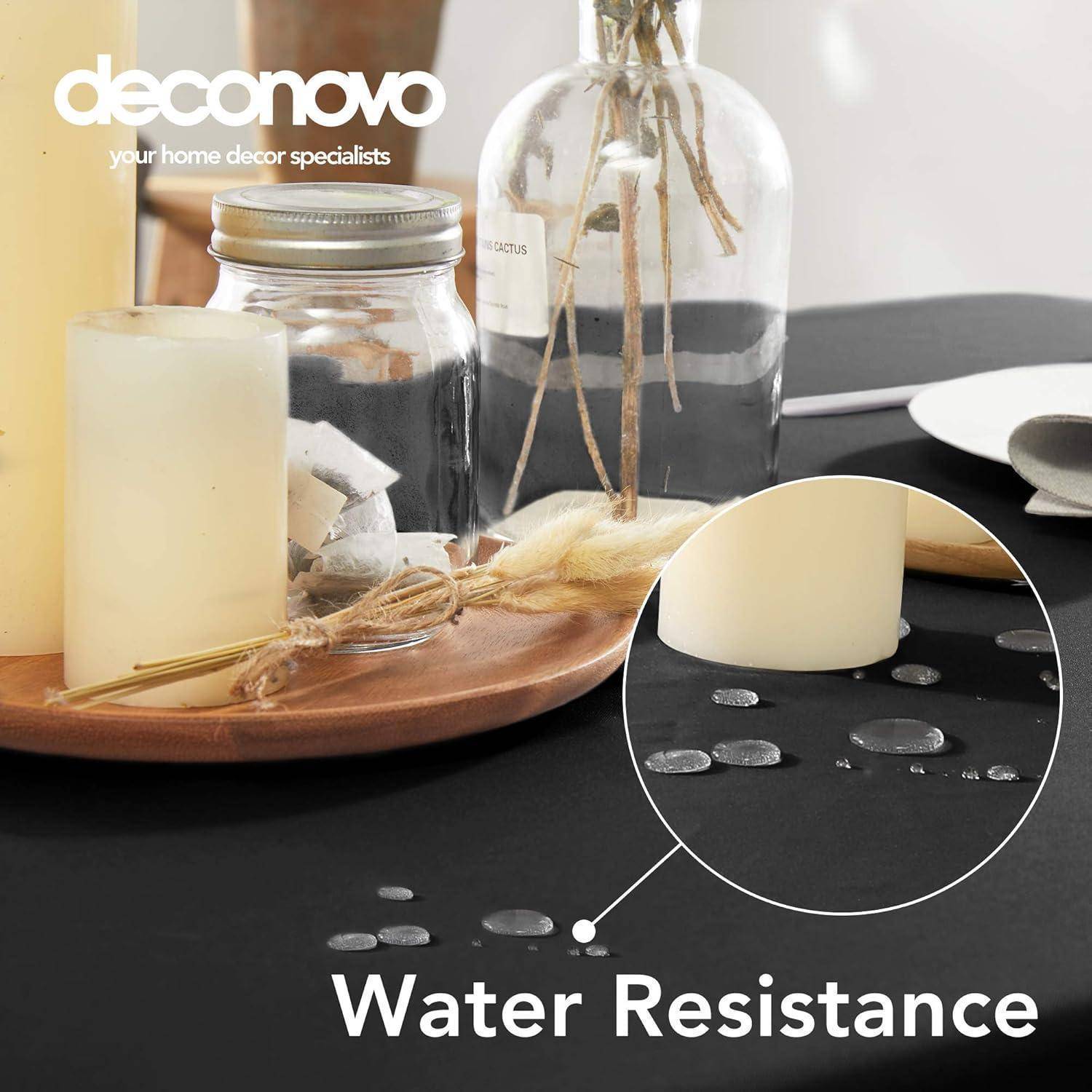 Ein Tisch mit einer schwarzen Stoffoberfläche zeigt Wassertropfen und eine Demonstration der Fleckenresistenz neben Kerzen und Dekorationsgegenständen.