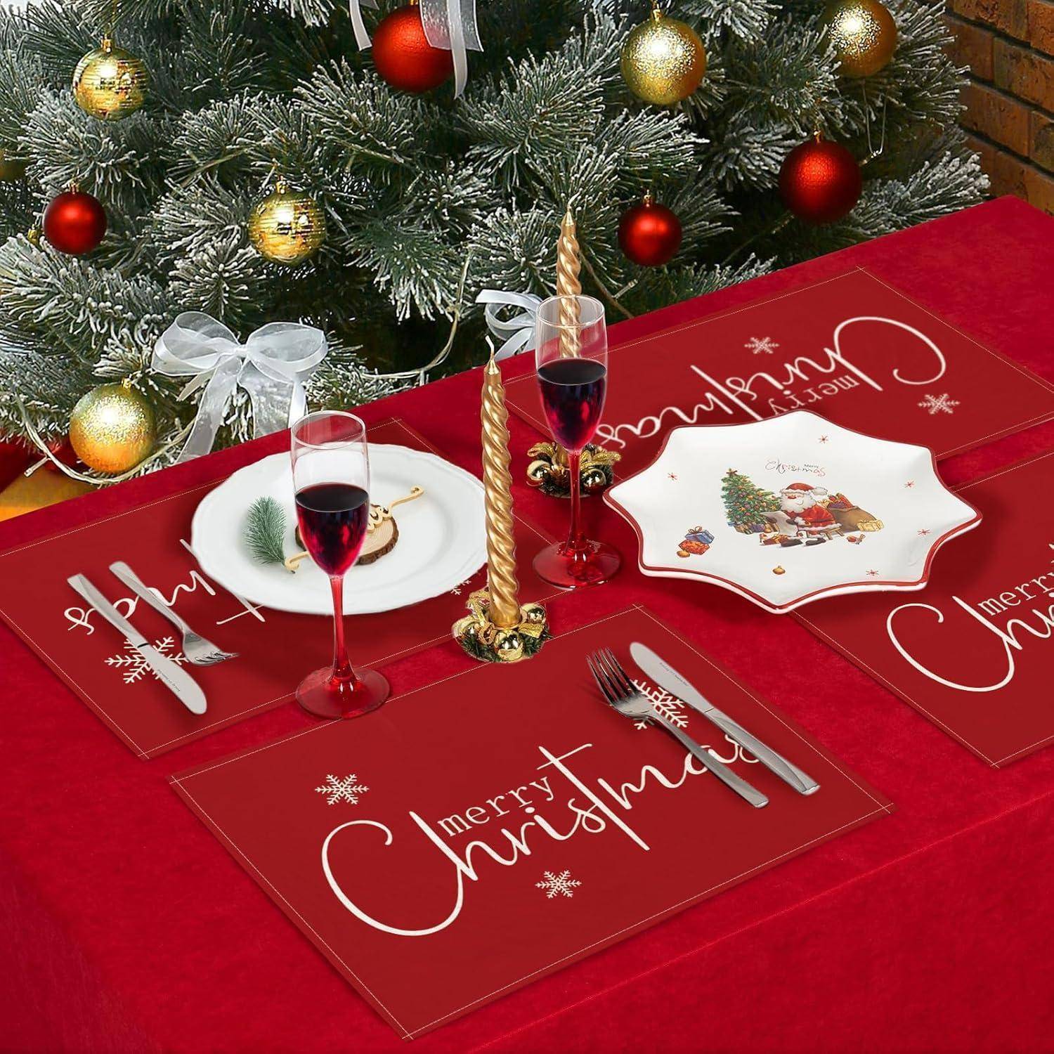 Ein weihnachtlich geschmückter Tisch mit roten Platzdeckchen, weißen Tellern und Gläsern Rotwein, aufgestellt neben einem Weihnachtsbaum mit Lichtern und Schmuck.