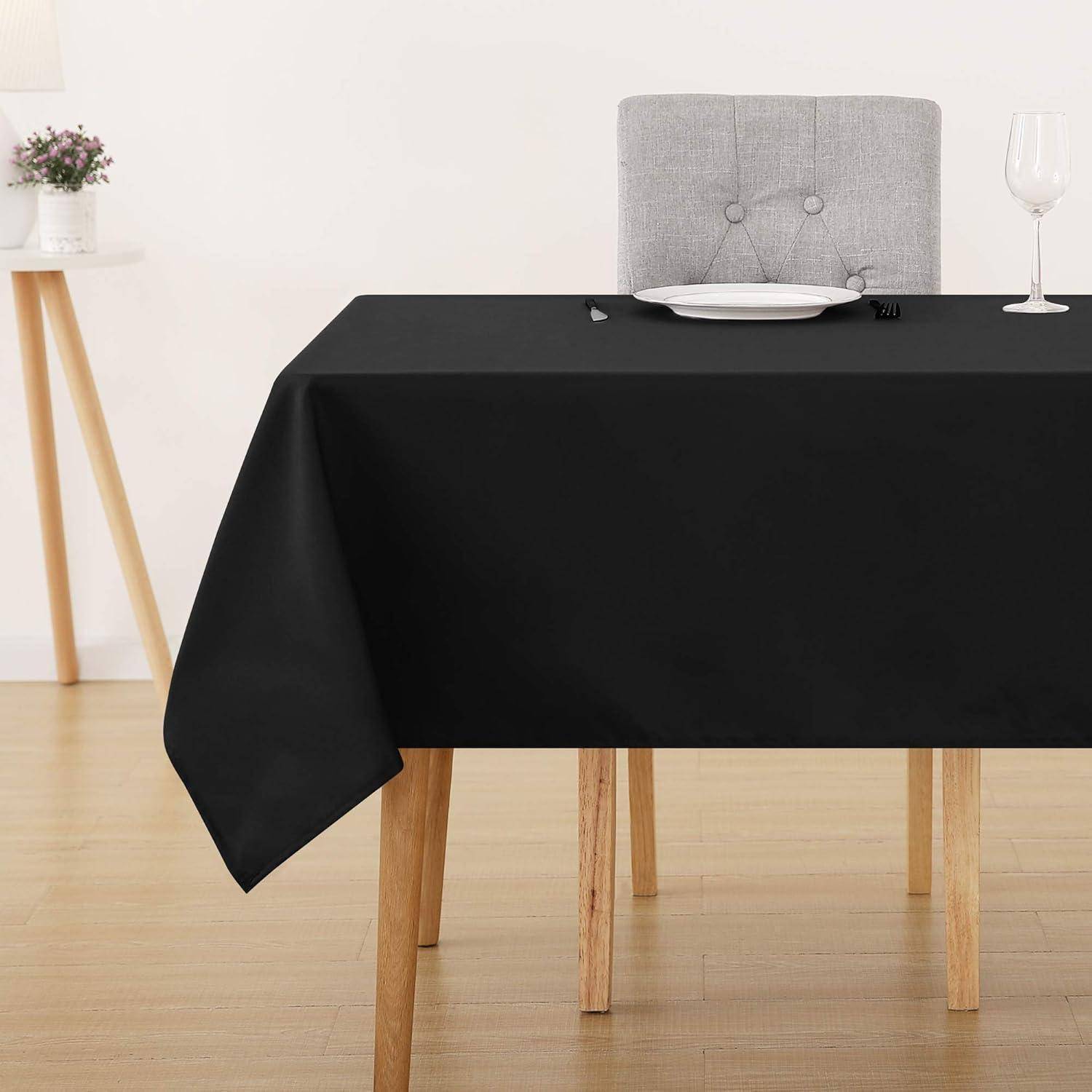 Ein Esstisch, der mit einer schwarzen Tischdecke, einem Stuhl, einem weißen Teller und einem Weinglas gedeckt ist, mit einer kleinen Pflanze auf einem Seitenhocker im Hintergrund.