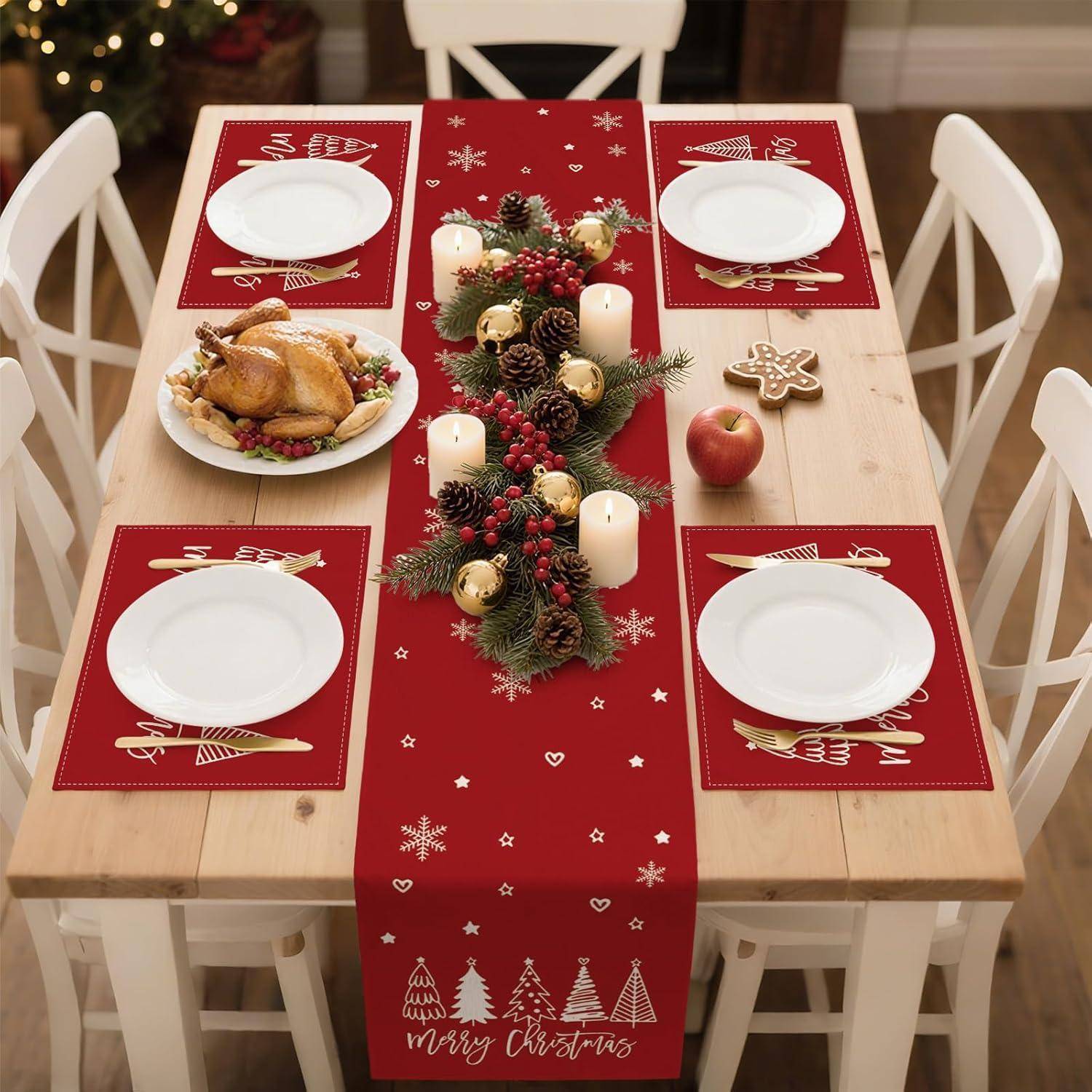 Ein hölzerner Esstisch, für Weihnachten gedeckt mit roten Platzdeckchen und einem Läufer, Tellern, Besteck, dekorierten Kerzen, Tannenzapfen und Weihnachtsschmuck.