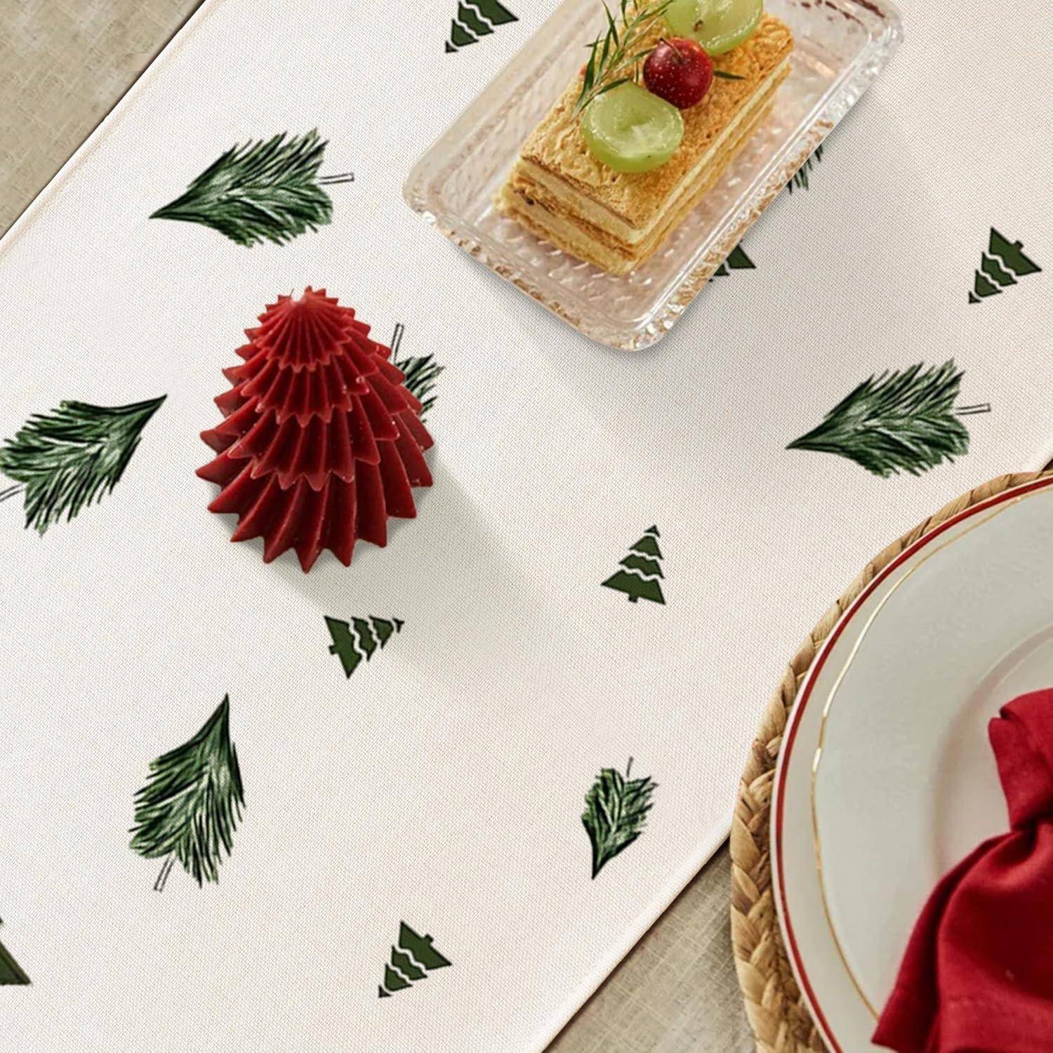 Eine festliche Tischdekoration mit einem weißen Läufer mit grünen Tannenmotiven, einer roten Papierbaumdekoration und einem Teller mit geschichteter Torte, die mit Trauben und Beeren gekrönt ist.