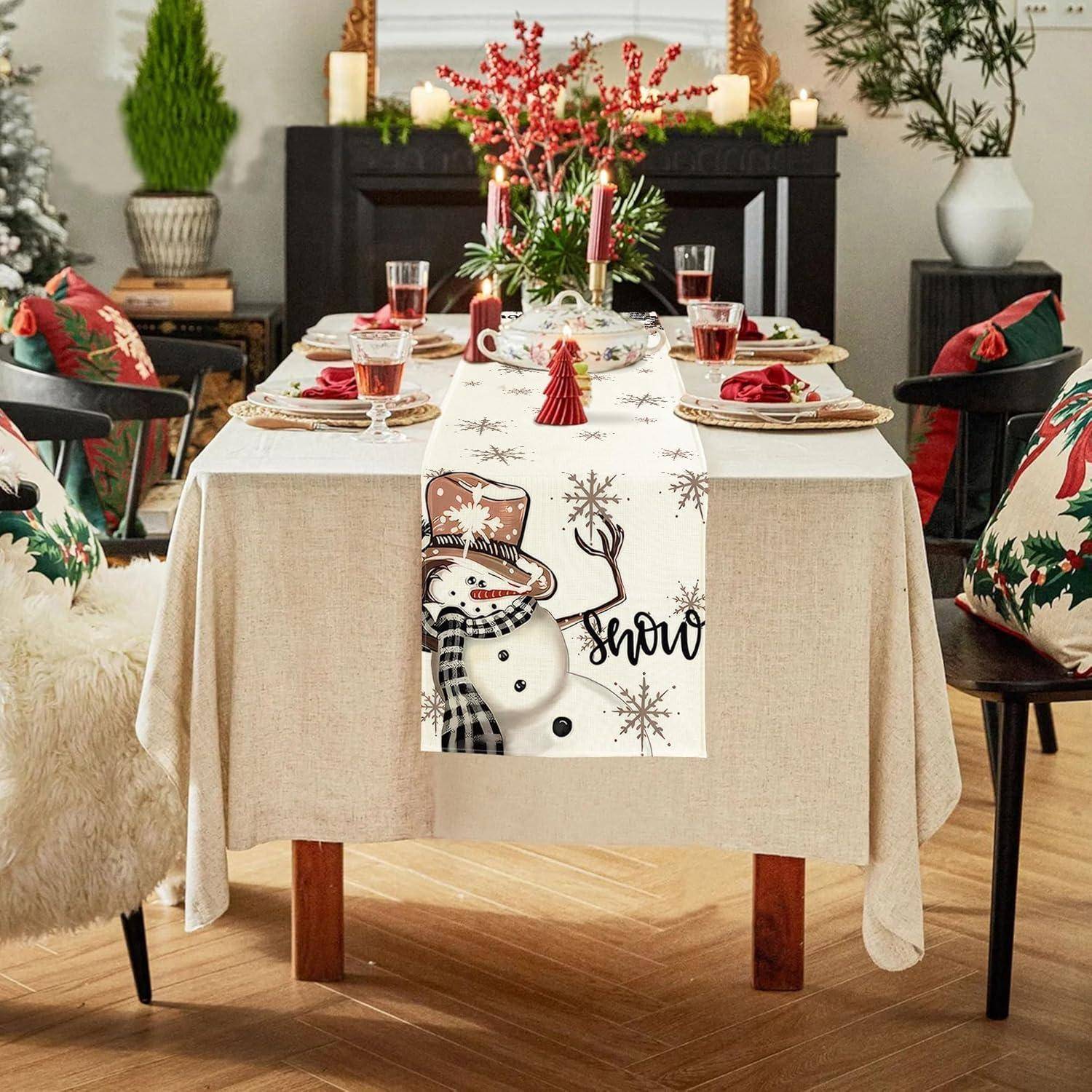 Ein festlich gedeckter Esstisch für ein Feiertagsessen, mit einer Schneemann-Tischdecke, roten Kerzen, Weingläsern und Weihnachtsdekoration.