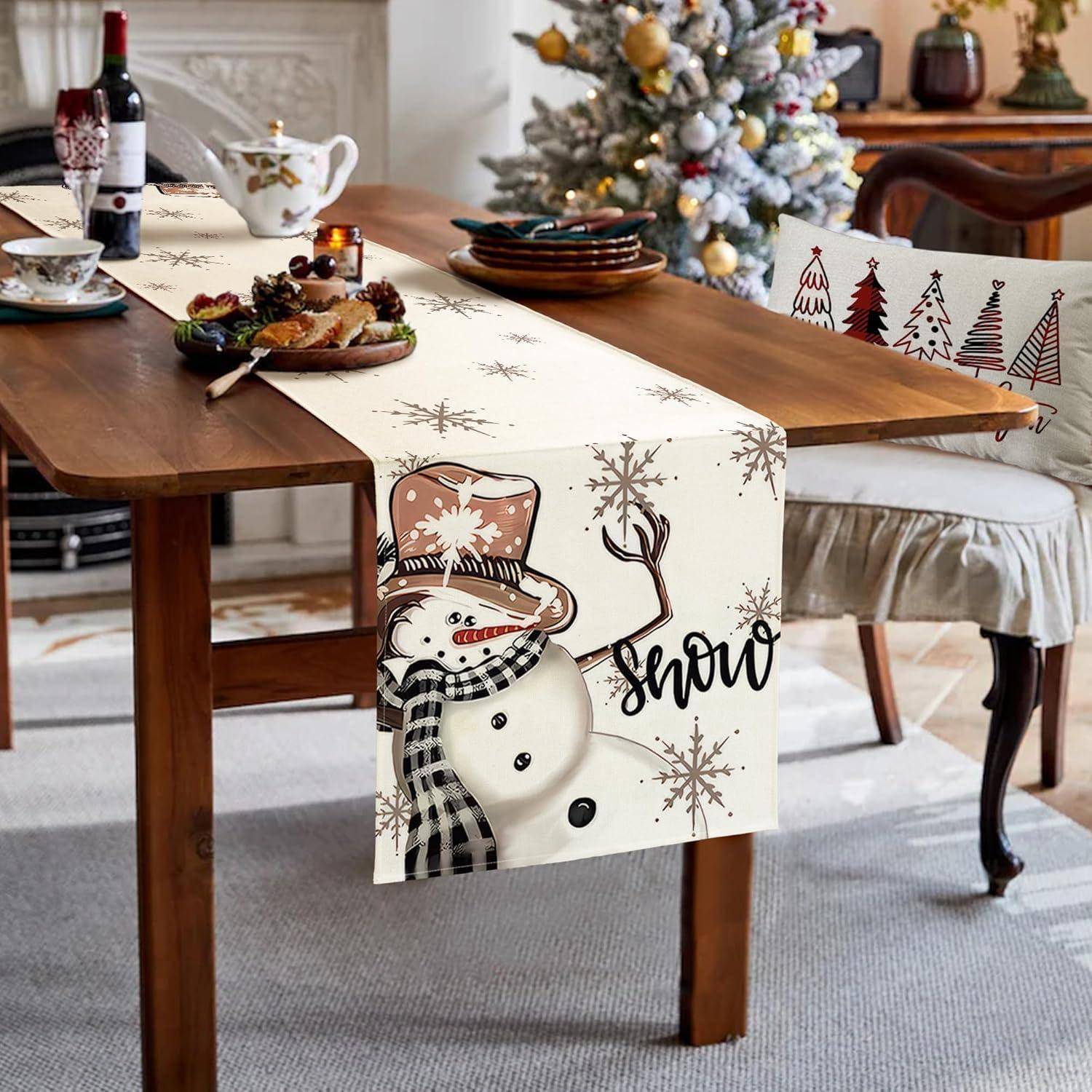 Ein Esstisch, der für Weihnachten dekoriert ist, mit einem Tischläufer mit Schneemann-Motiv und einem festlichen Weihnachtsbaum im Hintergrund.