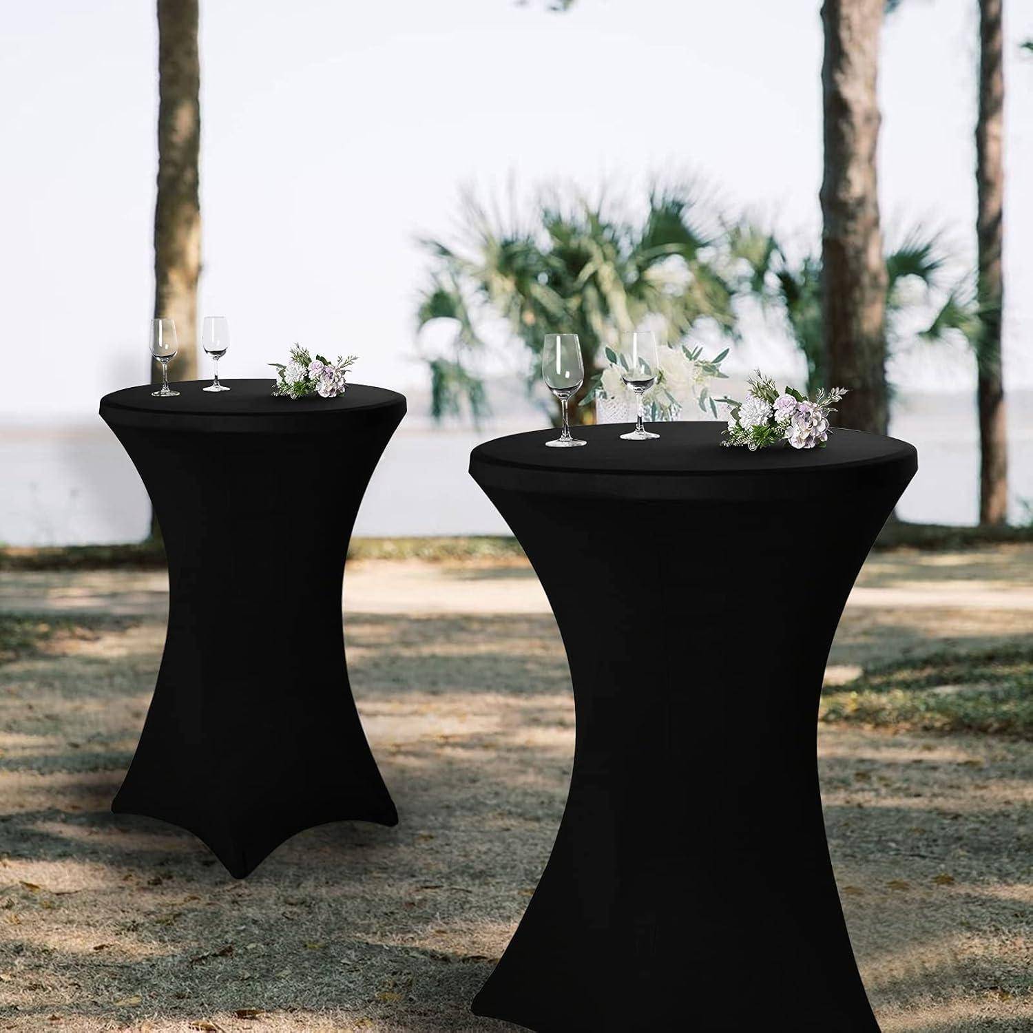 Zwei schwarze Cocktailtische im Freien, jeweils mit Gläsern und kleinen Blumenarrangements. Bäume und Grünpflanzen im Hintergrund.