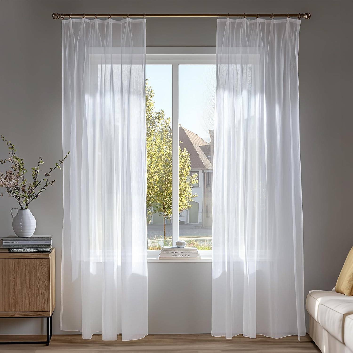Ein sonnendurchflutetes Fenster, umrahmt von weißen Vorhängen, mit Blick auf Bäume und Häuser draußen. Ein Holzschrank mit einer Vase und einer Pflanze steht in der Nähe.
