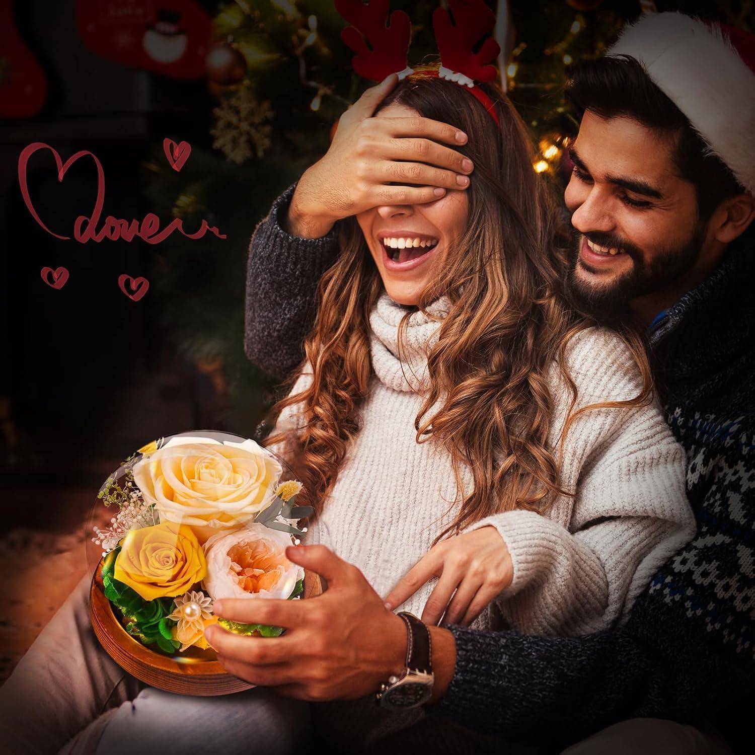 Eine Frau mit Rentierhörnern lächelt, während ihre Augen von der Hand eines Mannes verdeckt werden. Der Mann, der eine Weihnachtsmannmütze trägt, hält einen Blumenstrauß.