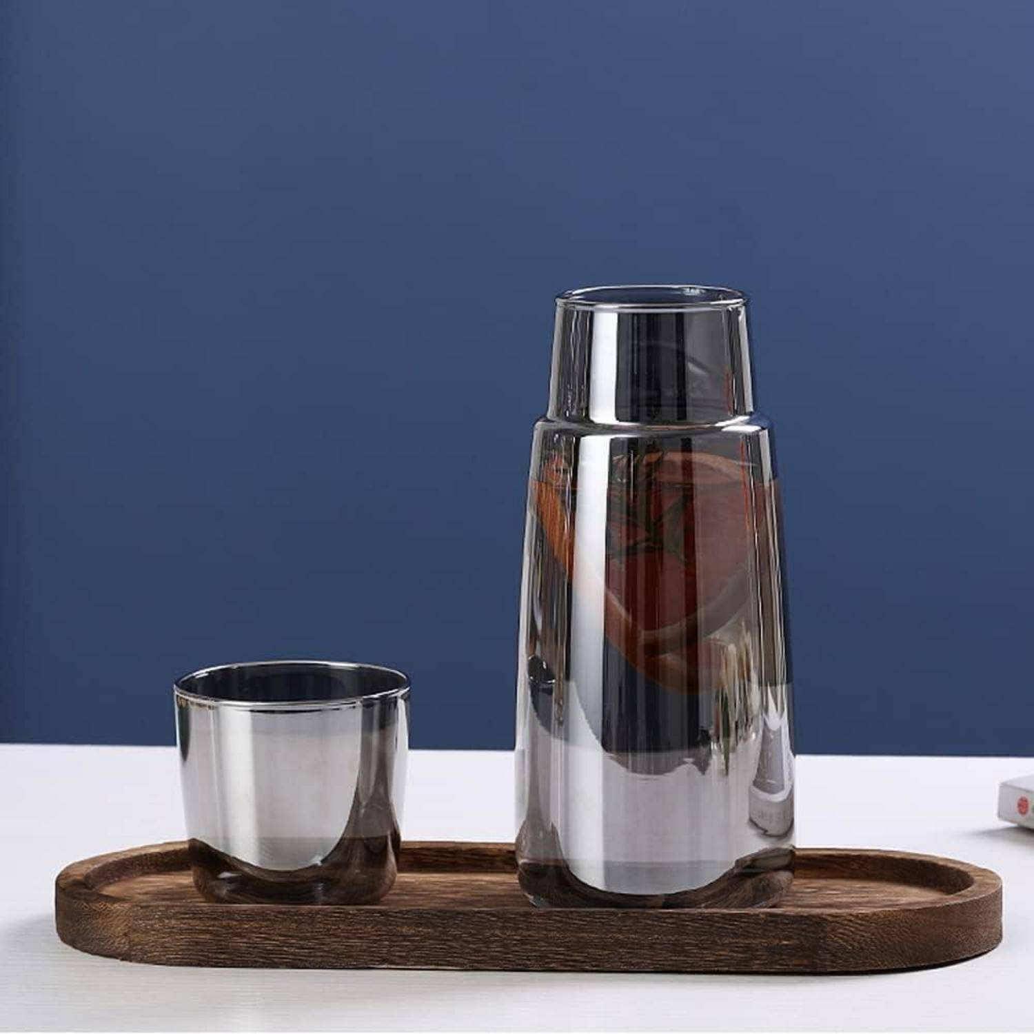 Eine Tasse und ein hoher Krug aus Edelstahl stehen auf einem Holztablett vor einem blauen Hintergrund und unterstreichen das moderne Design von Küchengeschirr.