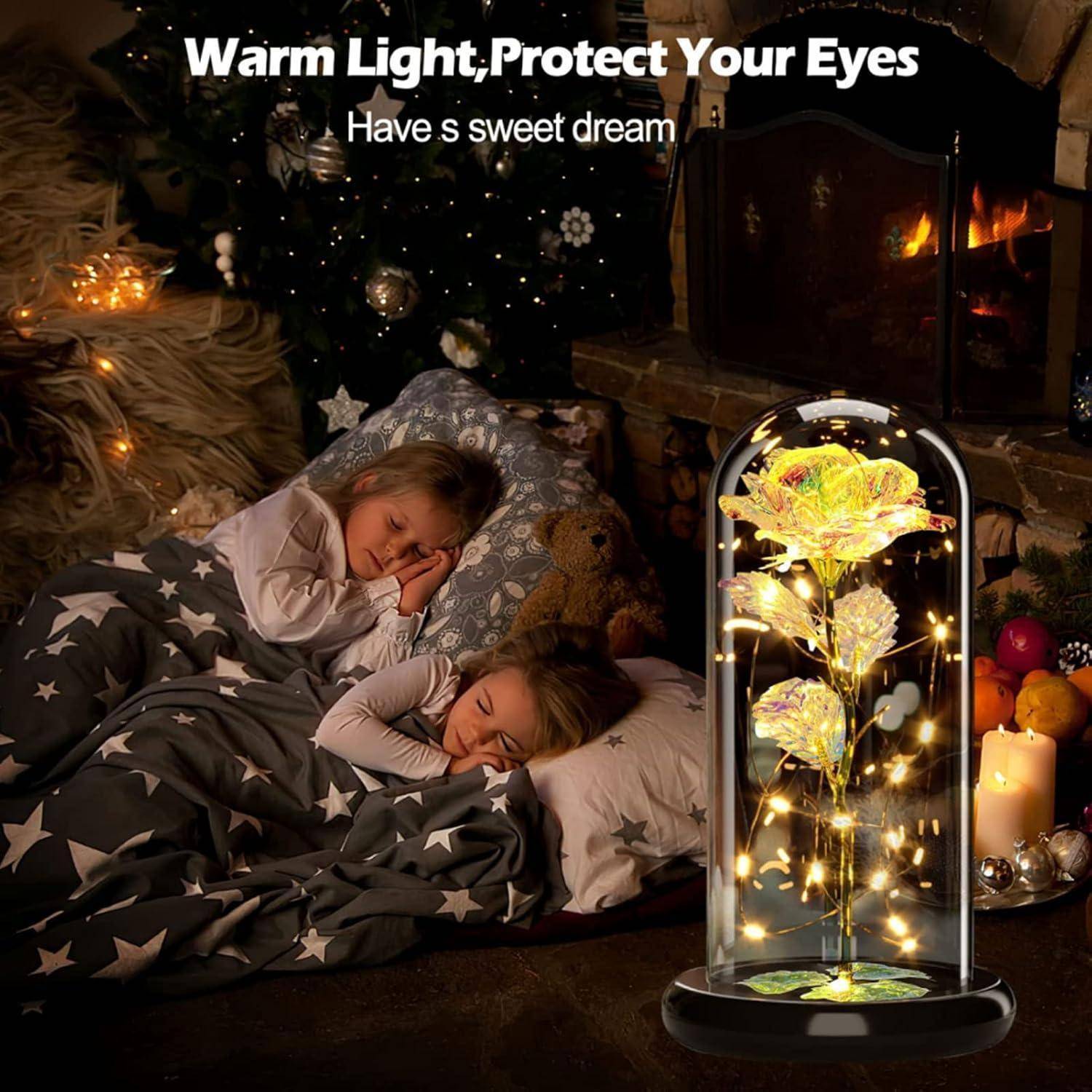 Zwei Kinder schlafen neben einem Kamin unter einer sternengemusterten Decke. Eine leuchtende Blumenlampe daneben sorgt für eine warme Atmosphäre. Text lautet: 