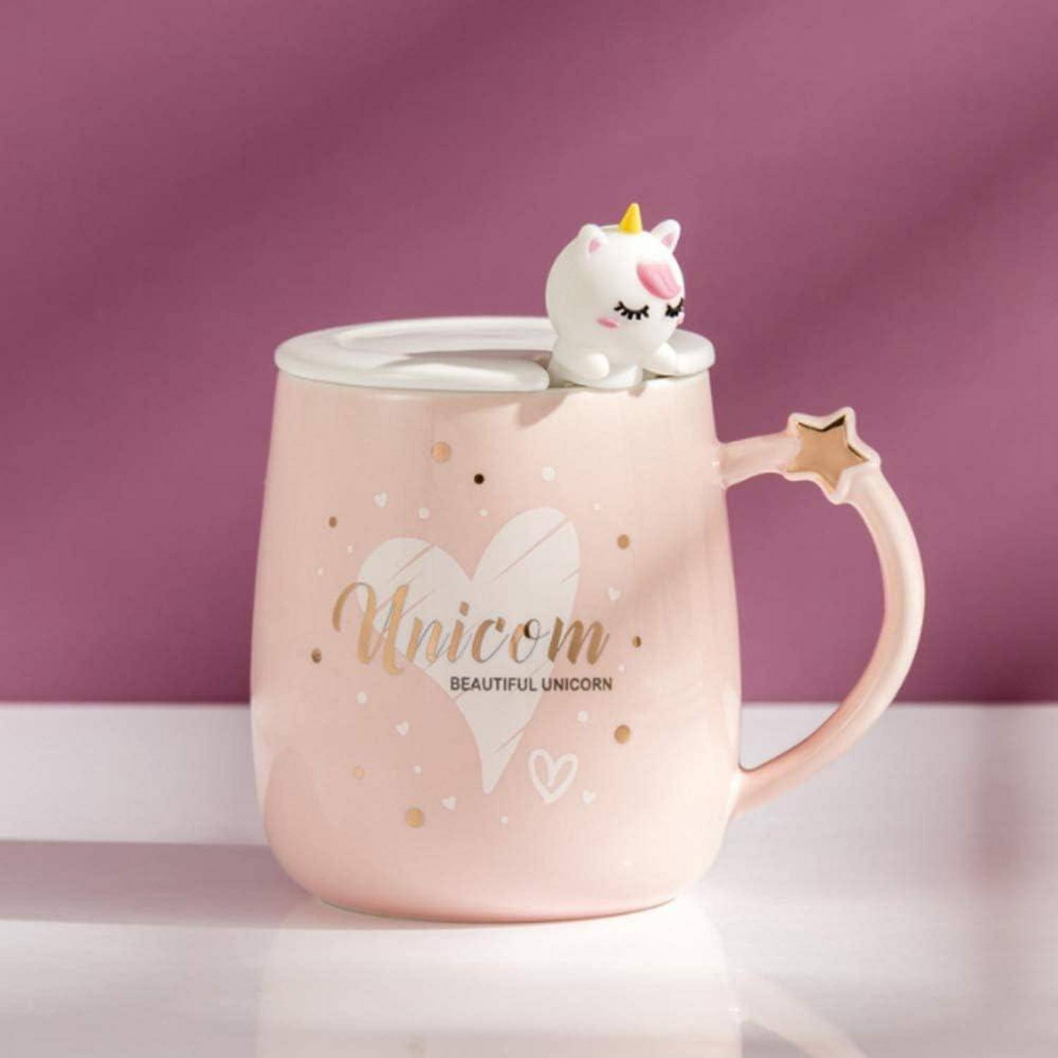 Eine rosa Tasse mit der Aufschrift 'Einhorn Wunderschönes Einhorn', mit einer Einhornfigur auf dem Deckel und einem Stern am Henkel, vor einem lila Hintergrund.