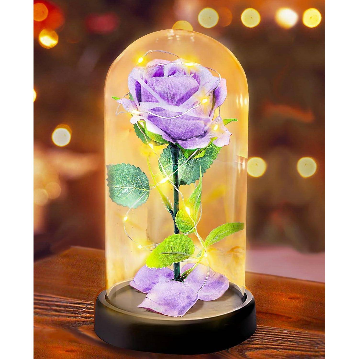 Eine lila Rose mit grünen Blättern in einer Glaskuppel, geschmückt mit kleinen leuchtenden Feenlichtern, steht auf einem Holztisch.