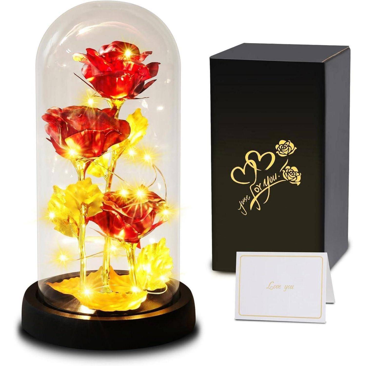Glaskuppel mit beleuchteten roten Rosen und goldenen Blättern. Daneben eine schwarze Box mit goldenem Herz und Rosenillustrationen sowie einer Karte mit der Aufschrift „Ich liebe dich