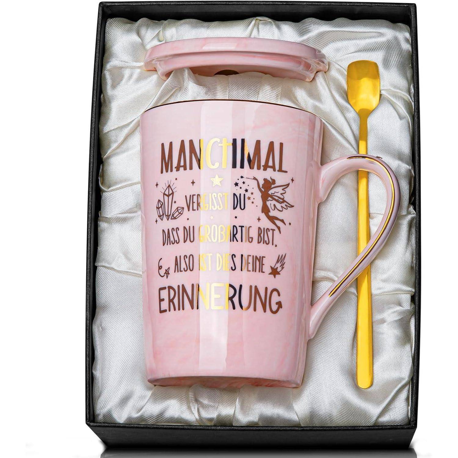 Eine rosa Keramiktasse in einer Geschenkbox mit einem goldenen Löffel. Die Tasse verfügt über deutschen Text und florale Designs.
