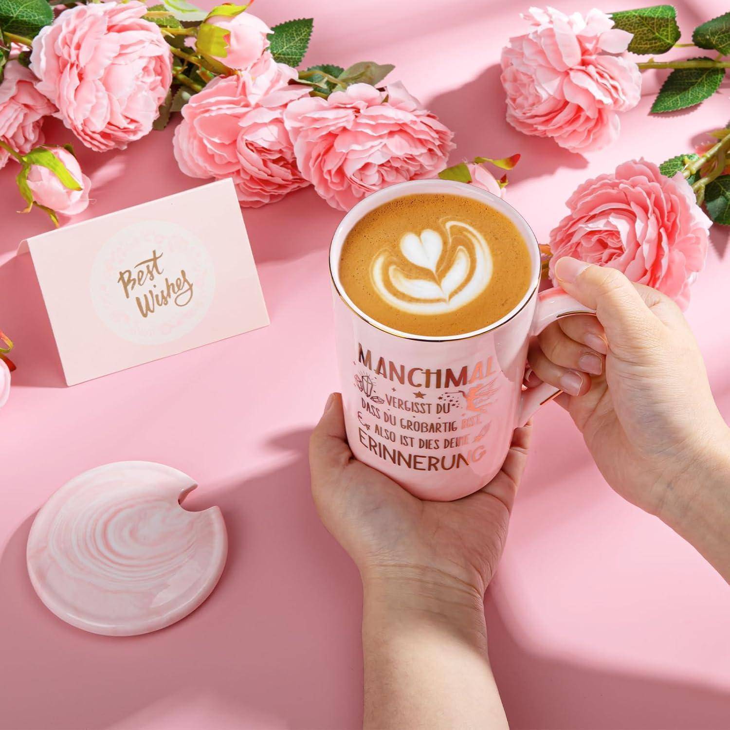 Eine Hand hält eine rosa Tasse mit Latte-Kunst zwischen rosa Rosen und einer Karte mit der Aufschrift 