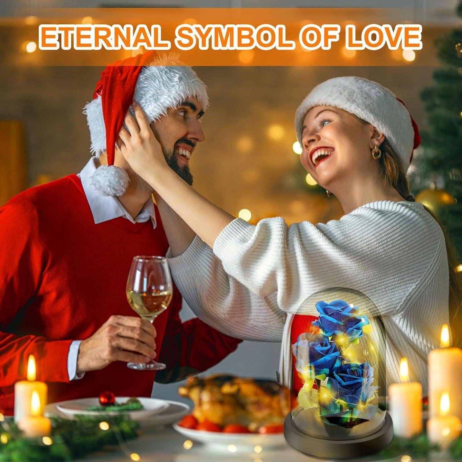Ein lächelndes Paar mit Weihnachtsmützen stößt mit Weingläsern an einem festlich geschmückten Tisch an, auf dem eine leuchtende Blumenornament prangt. Text lautet: ‚Ewiges Symbol der Liebe.