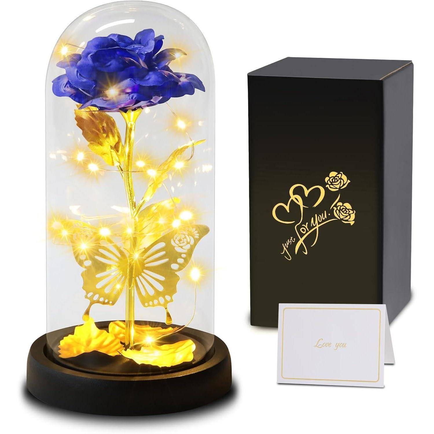 Eine blaue Rose in einer Glaskuppel, geschmückt mit goldenen Blättern, einem Schmetterling und Lichterketten. Daneben eine schwarze Box mit der Aufschrift ‚Love you' in goldener Schrift.
