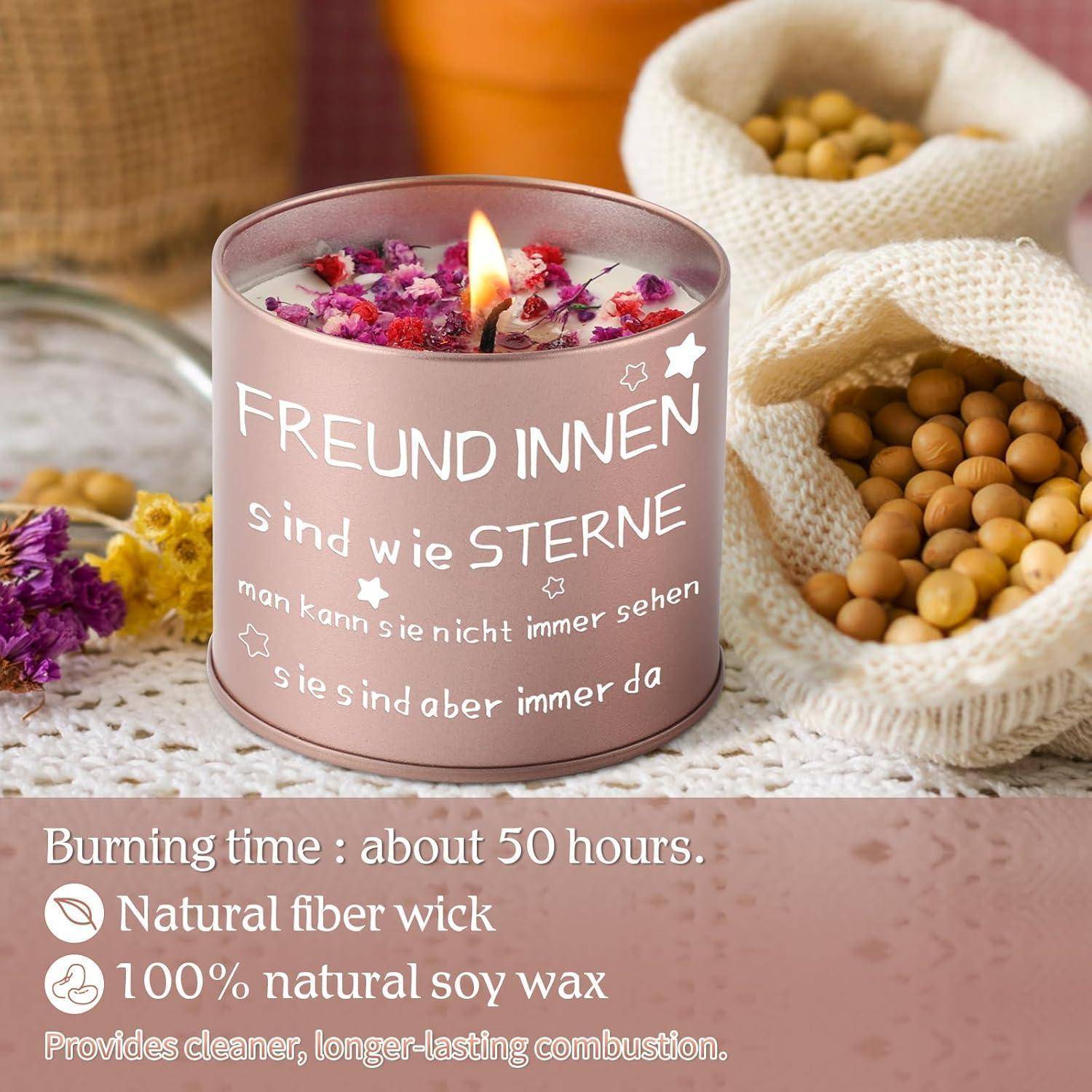 Eine brennende Kerze mit deutschem Text über Freundschaft ist umgeben von lila Blumen und Holzschalen. Der Text darunter hebt die Eigenschaften der Kerze hervor: 50 Stunden Brenndauer, Docht aus natürlichen Fasern und Sojawachs.