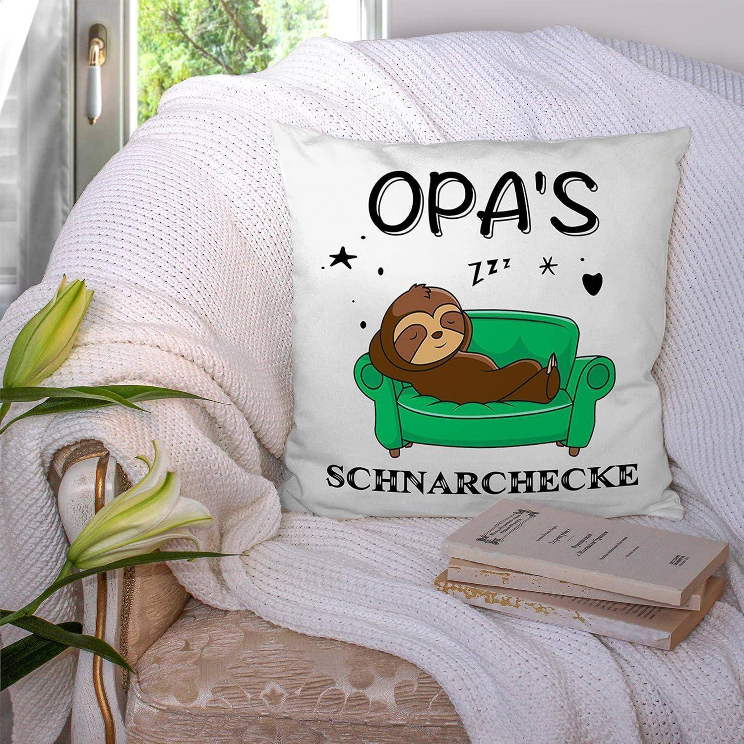 Ein Zierkissen auf einem gemütlichen Sofa zeigt einen Cartoon-Faultier, das auf einem grünen Sofa schläft. Der Text lautet 'OPA'S Schnarchecke', umgeben von Sternen.