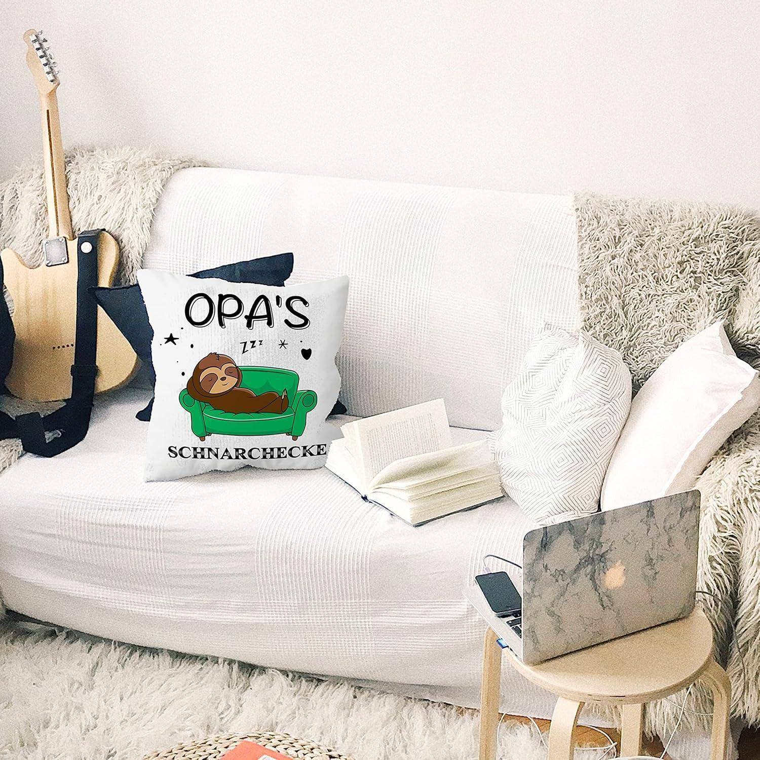 Ein gemütliches Wohnzimmer mit einem weißen Sofa, einer Gitarre und einem offenen Laptop auf einem kleinen Tisch. Ein Kissen trägt die Aufschrift „Opa's Schnarchecke
