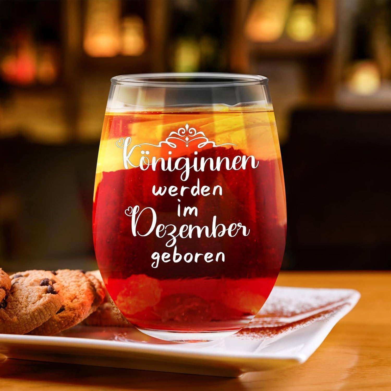 Ein Glas mit rotem Getränk und Zitrusscheiben steht auf einem Teller neben Keksen. Der Text auf dem Glas lautet: „Königinnen werden im Dezember geboren.