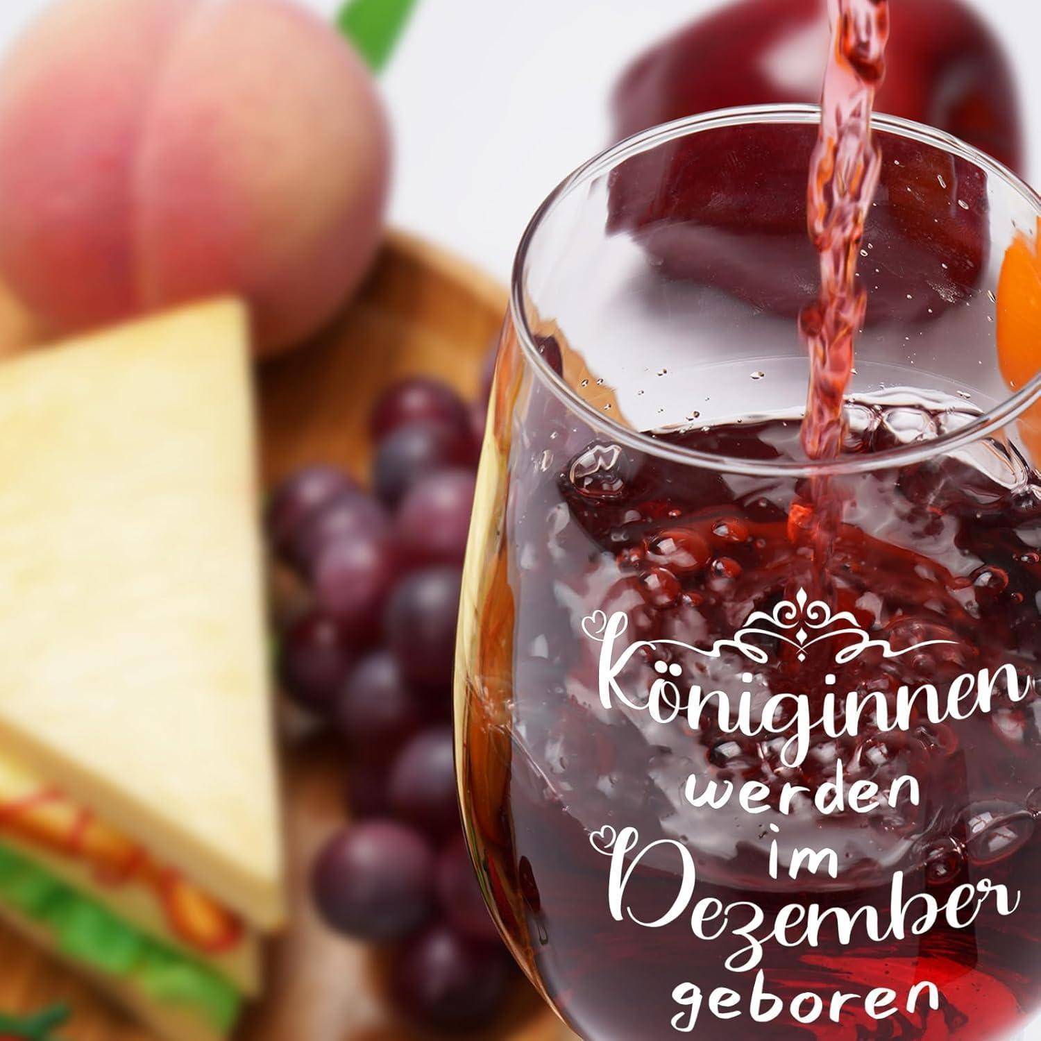 Ein Glas Rotwein wird eingeschenkt. Trauben und eine Käseplatte befinden sich im Hintergrund. Das Glas trägt den Text 