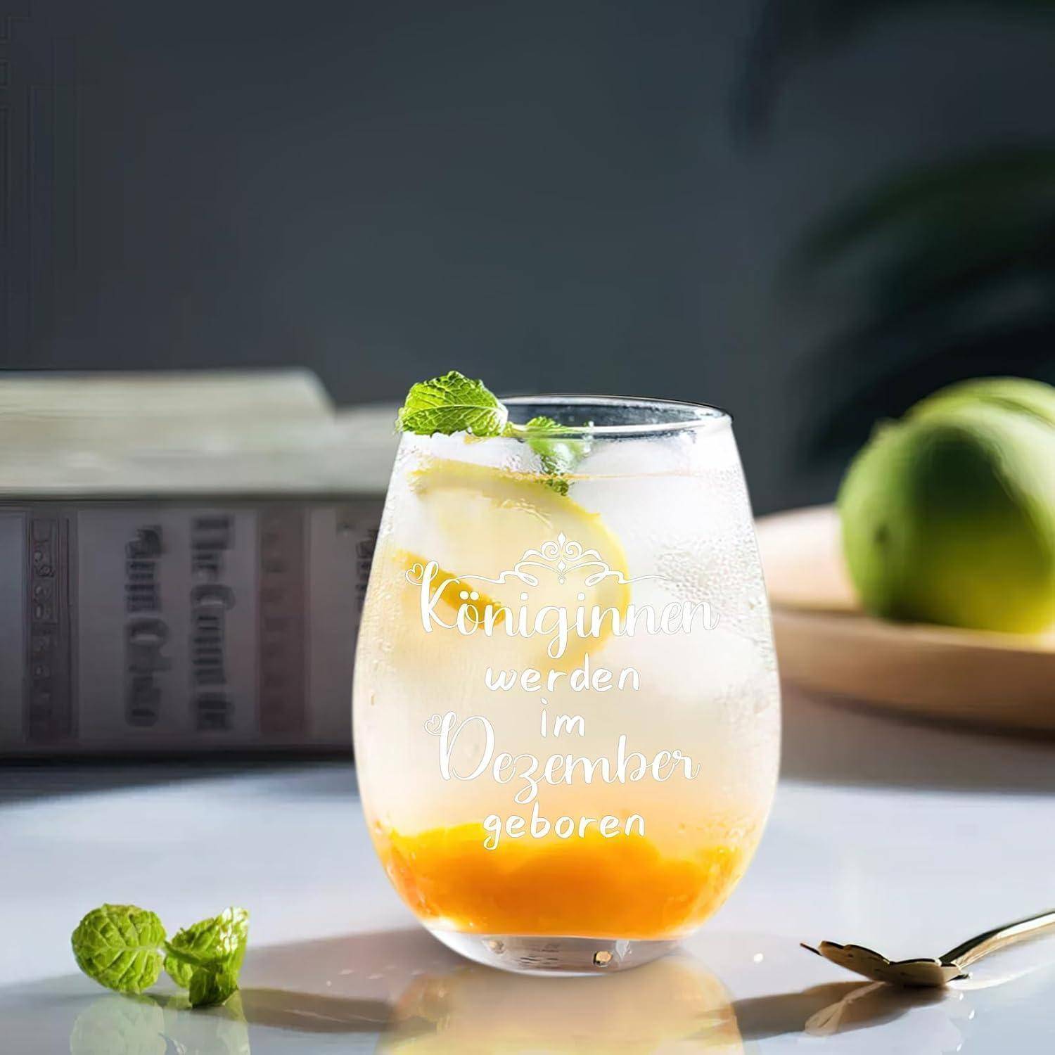 Ein klares Glas mit einem orangefarbenen Getränk und Minze, das auf einem Tisch steht. Ein Buch und eine Limette liegen daneben. Deutscher Text auf dem Glas.