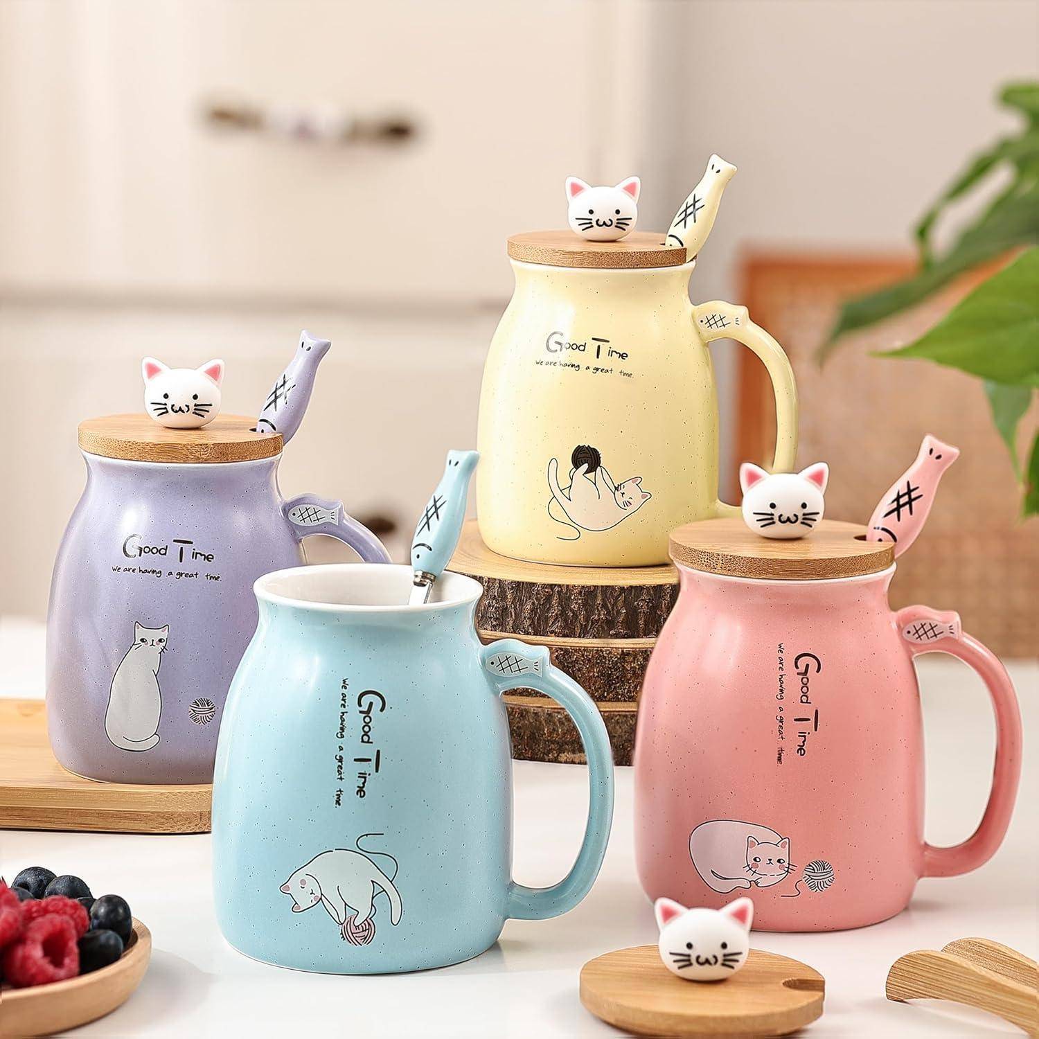 Drei Keramikbecher mit Katzendesigns und passenden Deckeln, die kleine Katzenfiguren enthalten, stehen auf einem Tisch. Jeder Becher ist in einer anderen Farbe gehalten.