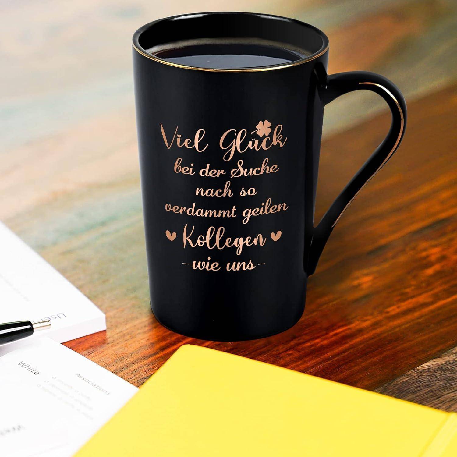Eine schwarze Kaffeetasse mit goldener Schrift, auf der "Viel Glück bei der Suche nach so verdammt geilen Kollegen wie uns."" steht, ruht auf einem Tisch.