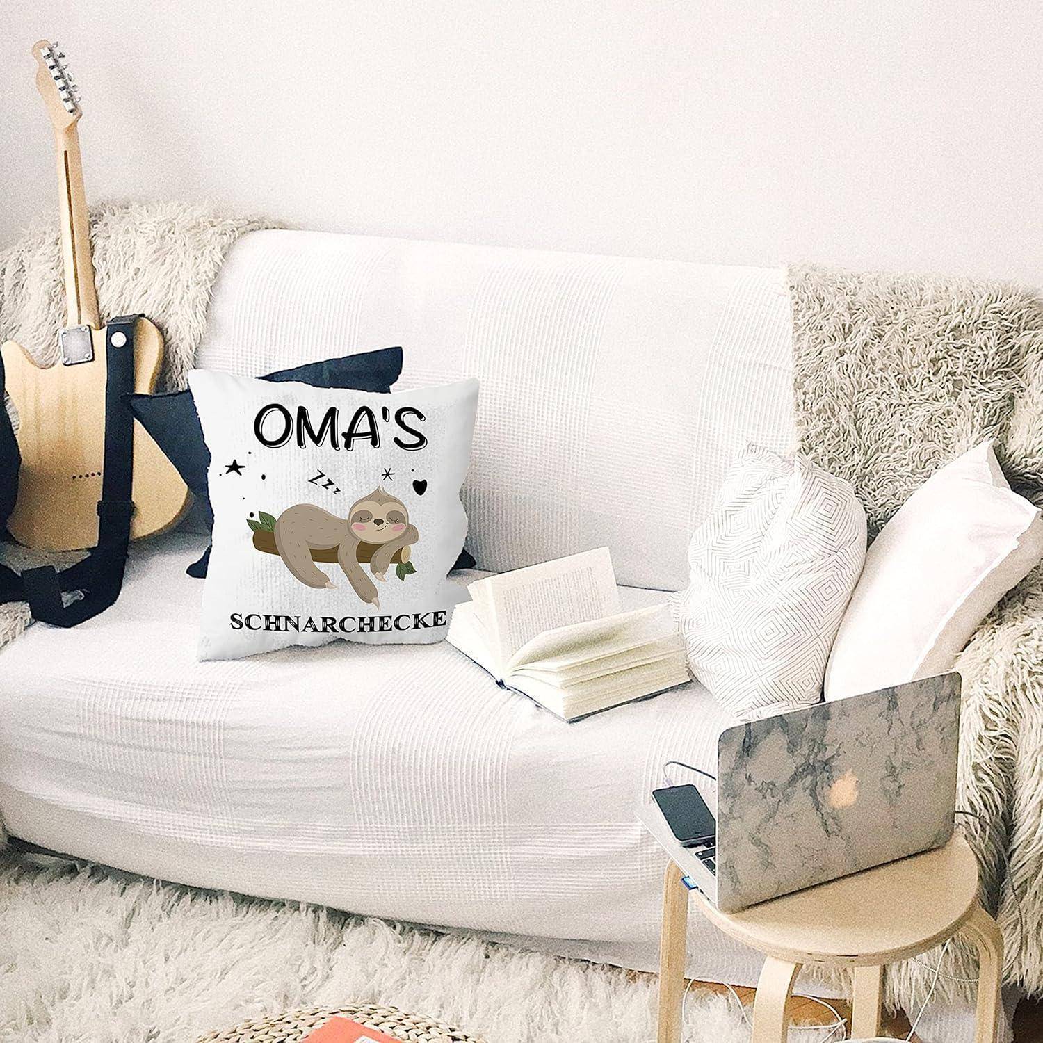 Gemütliches Wohnzimmer mit einem weißen Sofa, einer Gitarre und einem offenen Laptop auf einem kleinen Tisch. Ein Kissen mit dem Design 'Oma's Schnarchecke' liegt auf dem Sofa.