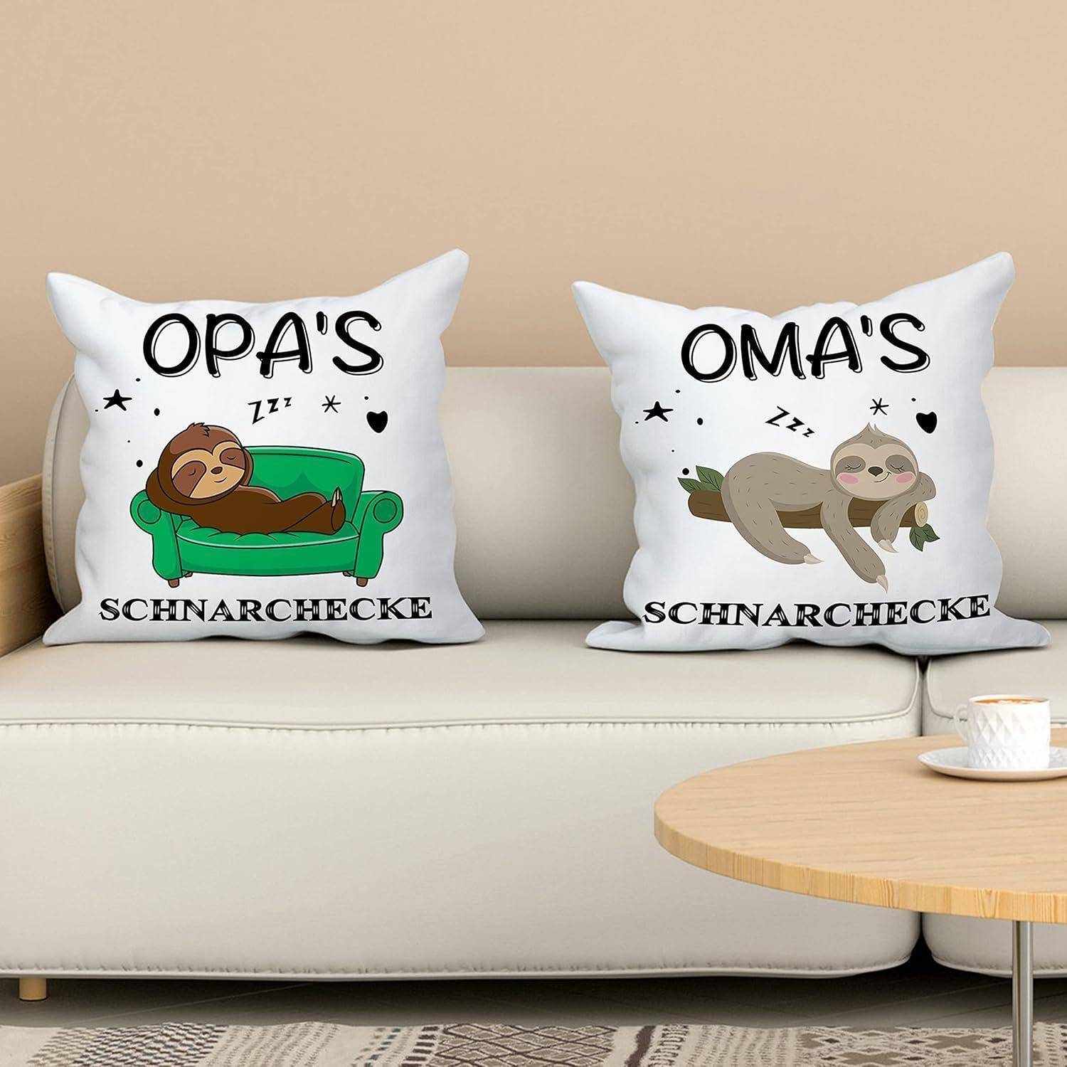 Zwei Kissen auf einem Sofa; links steht 'OPA'S Schnarchecke' mit einem schlafenden Faultier, rechts steht 'OMA'S Schnarchecke' mit einem liegenden Faultier.