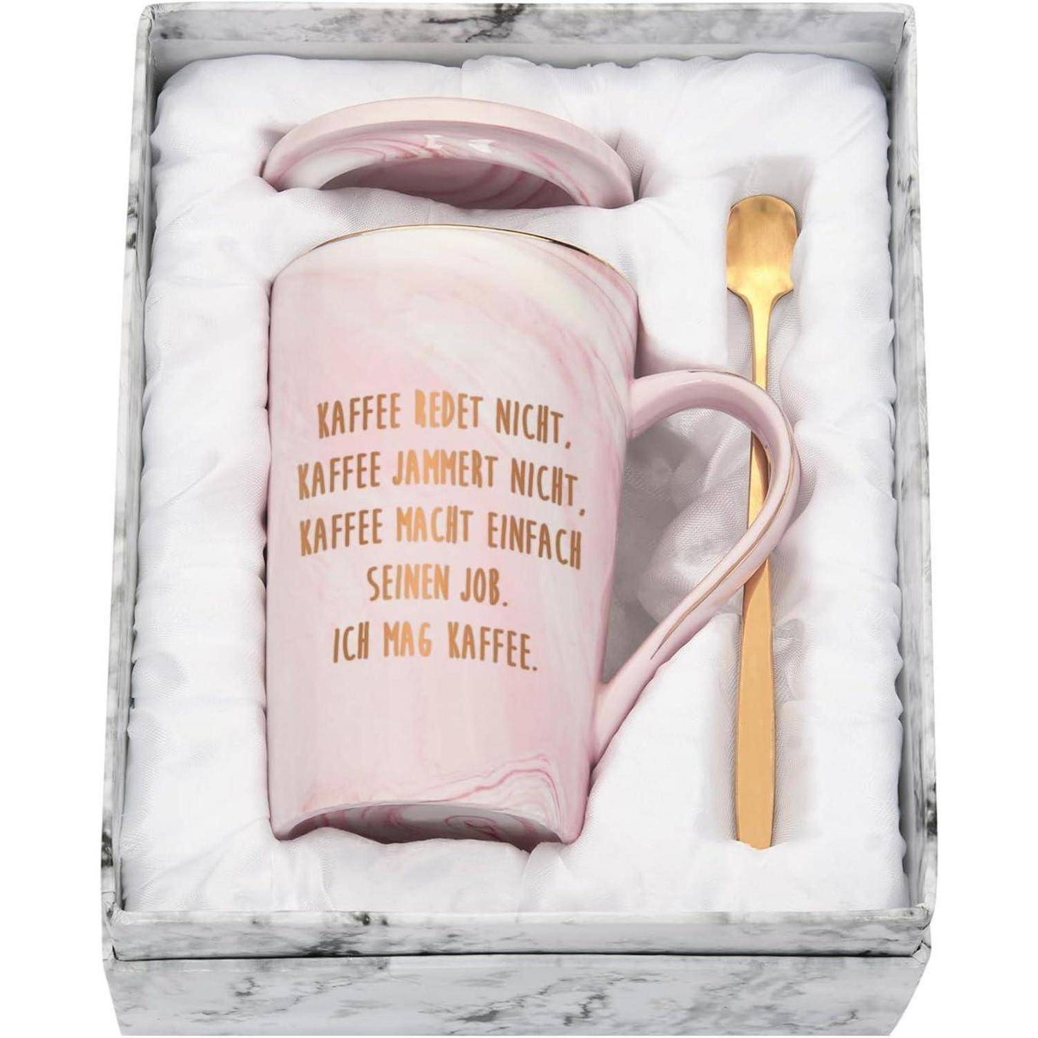 Ein rosa Becher mit goldener Schrift auf Deutsch steht in einer Box mit einem goldenen Löffel. Text lautet: 'Kaffee redet nicht. Kaffee jammert nicht. Kaffee macht einfach seinen Job. Ich mag Kaffee.