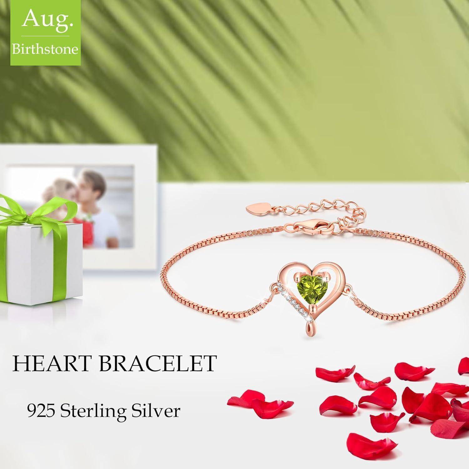 Ein silbernes Herzarmband mit einem grünen Edelstein auf einer Geschenkbox, umgeben von roten Blütenblättern. Text lautet '925 Sterling Silber' und 'Aug. Geburtsstein.