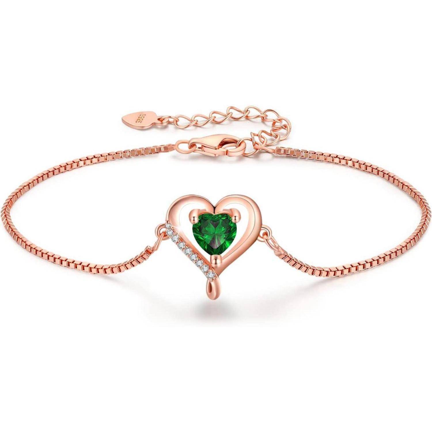 Ein roségoldenes Armband mit einem zentralen herzförmigen Design, in dem ein grüner Edelstein eingesetzt ist, verziert mit kleinen klaren Steinen und einer feinen Kette.