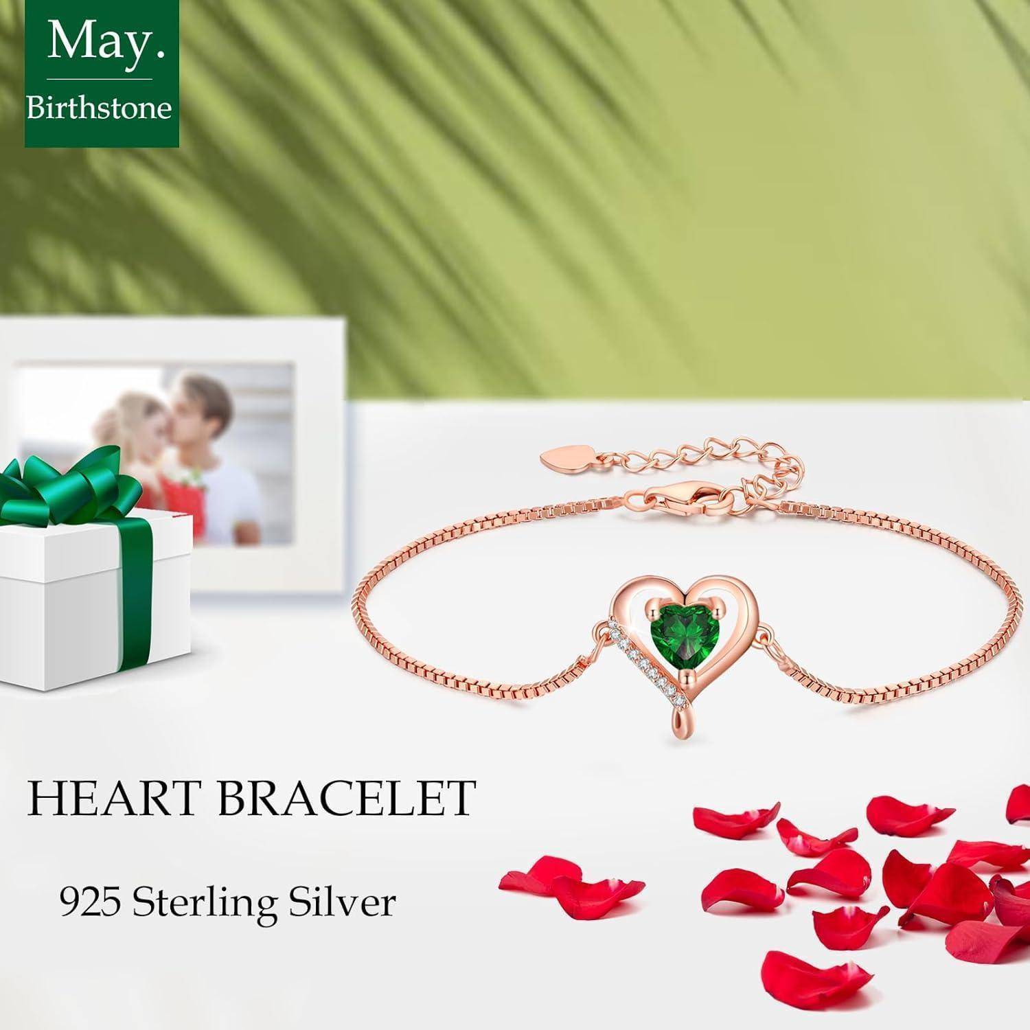 Herzarmband mit grünem Edelstein in der Mitte, umgeben von roten Rosenblütenblättern. Text lautet '925 Sterling Silber'. Eine verpackte Geschenkbox befindet sich im Hintergrund.