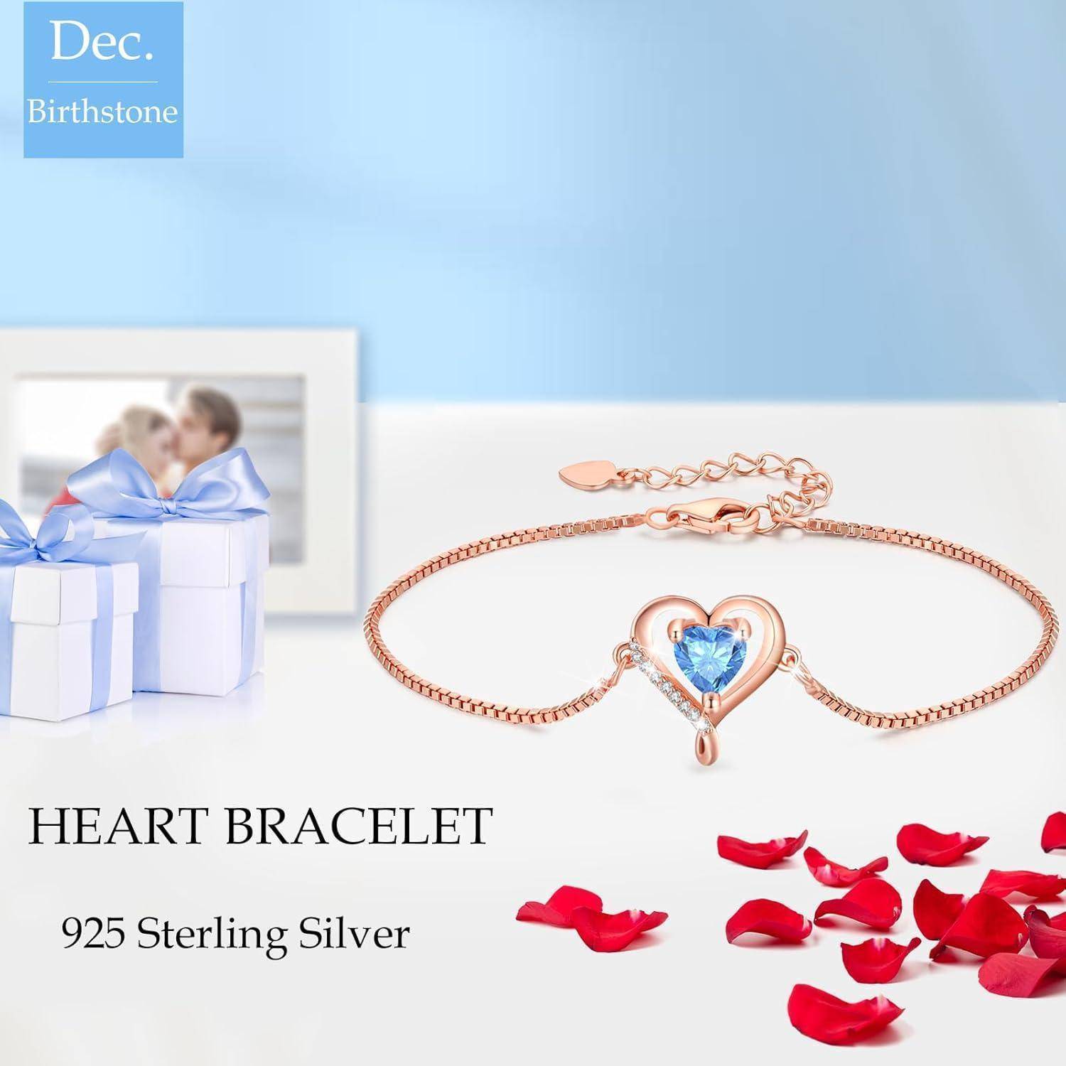 Eine Herzarmband mit einem blauen Edelstein als Mittelpunkt wird präsentiert. Der Text lautet '925 Sterlingsilber.' Eine Geschenkbox und verstreute Rosenblütenblätter befinden sich in der Nähe.