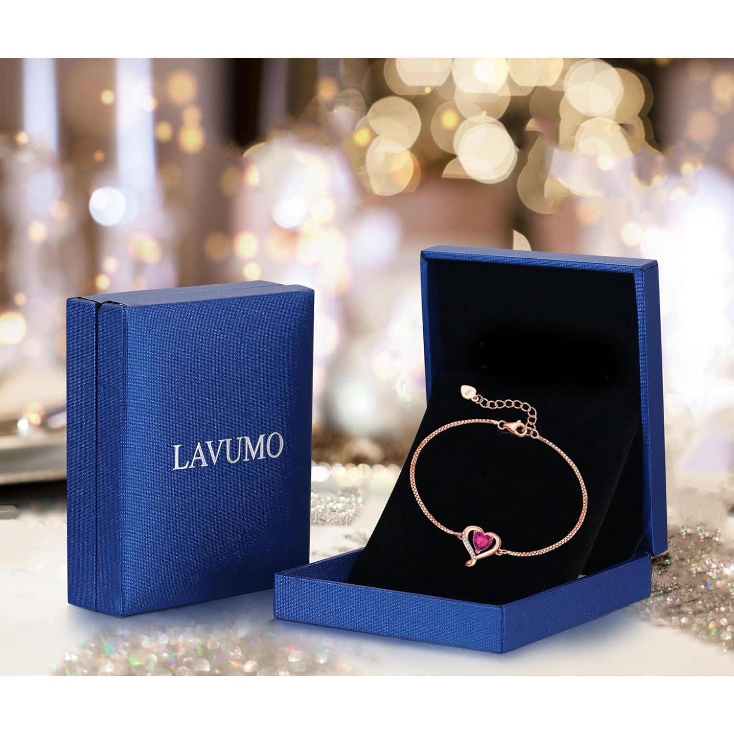Ein roségoldenes Armband mit einem herz-förmigen Anhänger liegt in einer offenen blauen Lavumo-Box, mit verschwommenen Lichtern im Hintergrund.