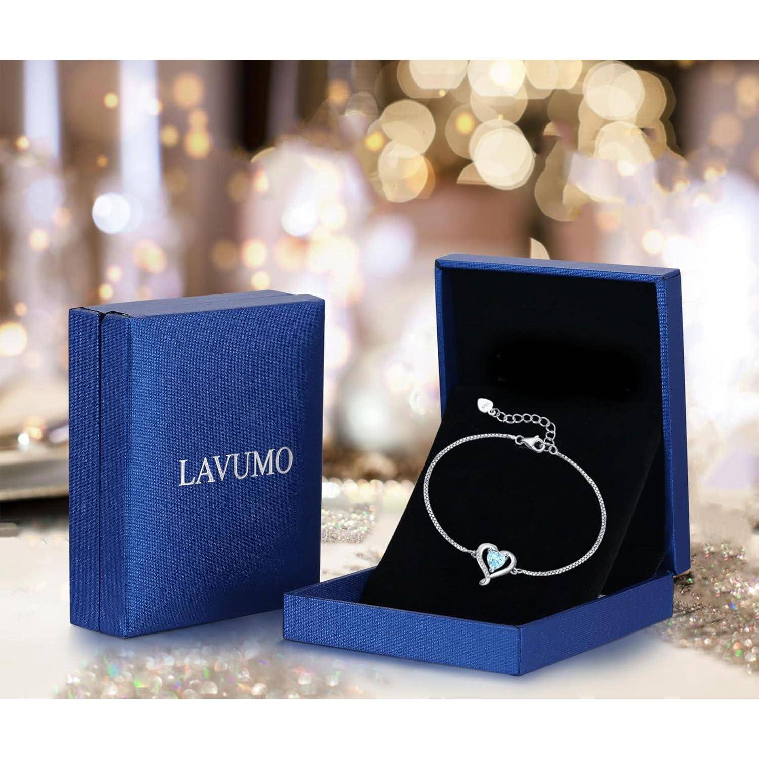 Ein zartes Armband mit einem Herz-Anhänger in einer offenen blauen Schatulle, neben einer geschlossenen Box mit der Aufschrift 