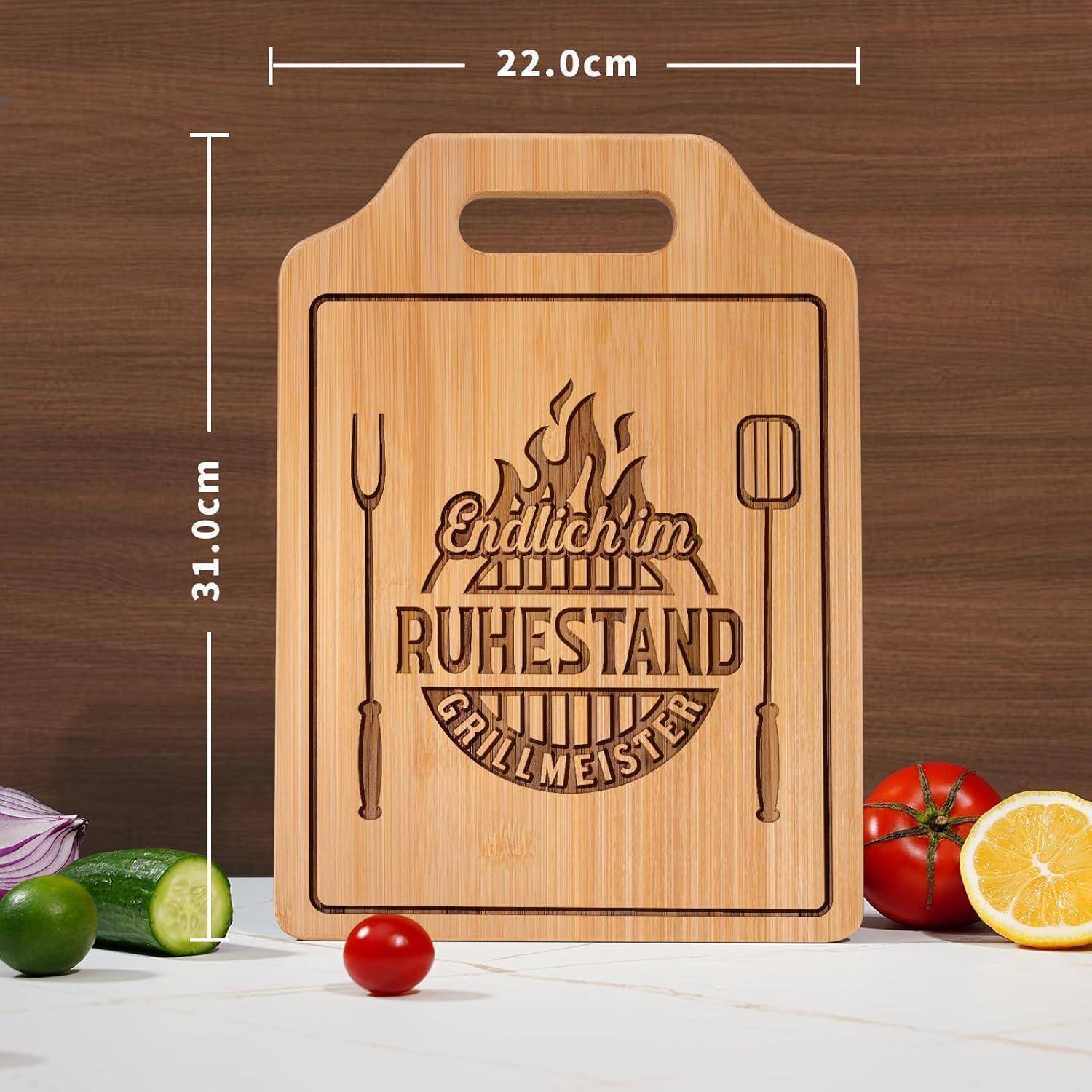 Holzschneidebrett mit der Gravur 'Endlich im Ruhestand Grillmeister', misst 22,0 cm x 31,0 cm, umgeben von Gemüse.