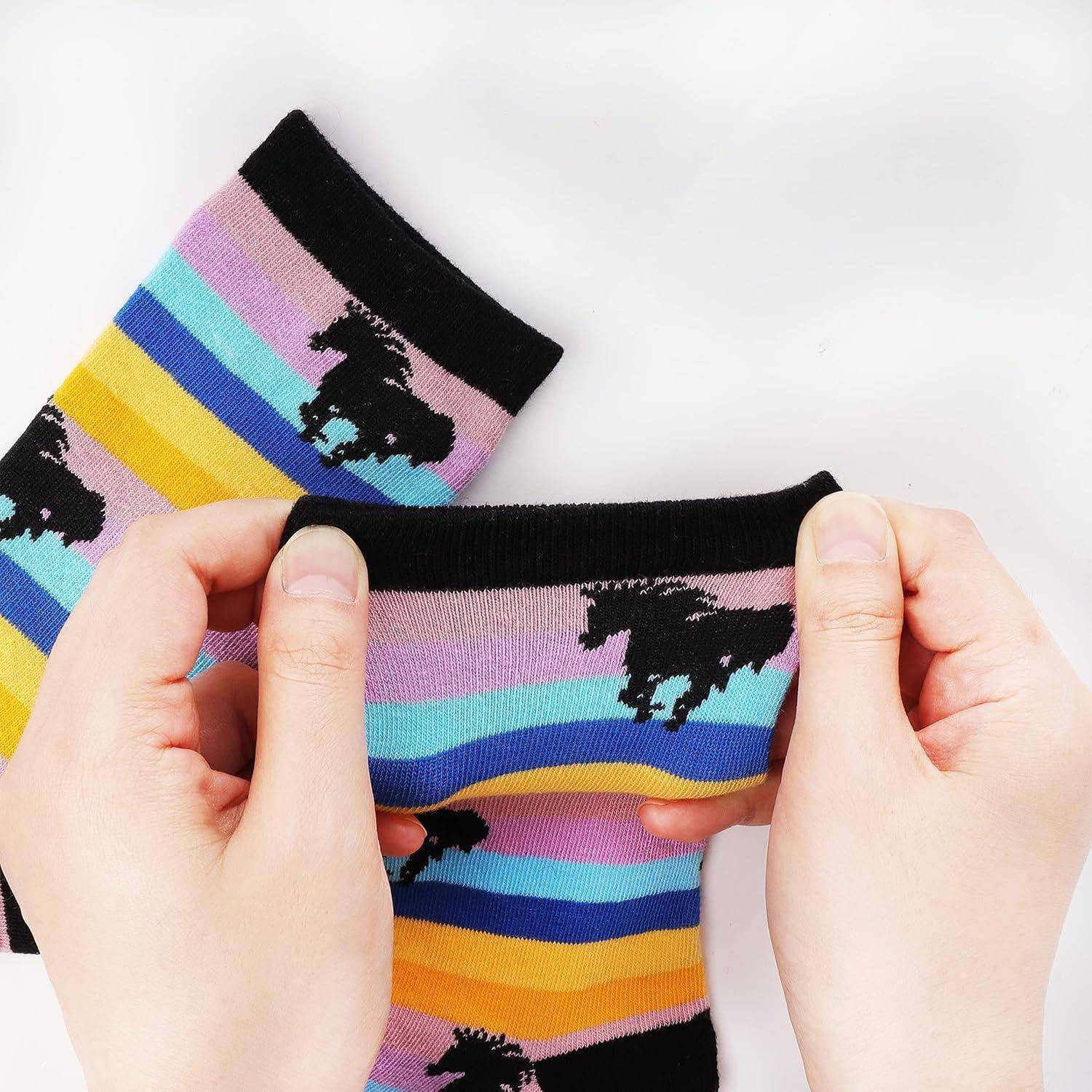 Hände, die bunte Socken mit einem schwarzen Pferdmuster halten und einen Regenbogen von horizontalen Streifen in Tönen von Rosa, Blau, Lila und Gelb zeigen.