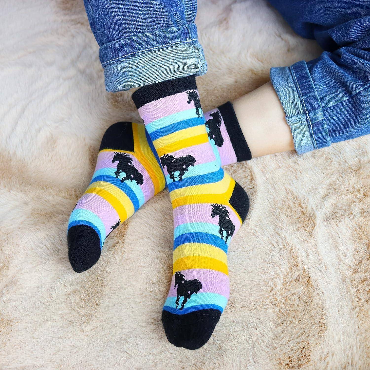 Person mit bunten gestreiften Socken mit Dinosaurier-Mustern, sitzt auf einer weichen, hellgefärbten Oberfläche, mit leicht hochgerollten Jeans.