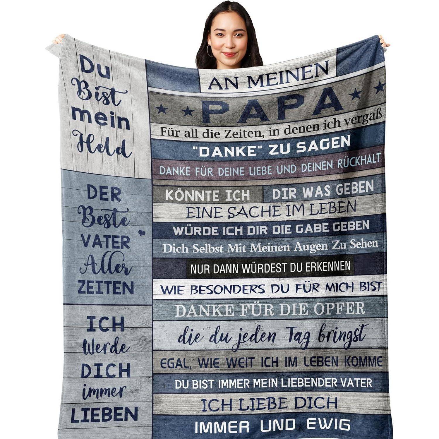 Eine Person hält eine Decke mit deutschem Text, der Liebe und Dankbarkeit für einen Vater ausdrückt und Wertschätzung und lebenslange Liebe hervorhebt.