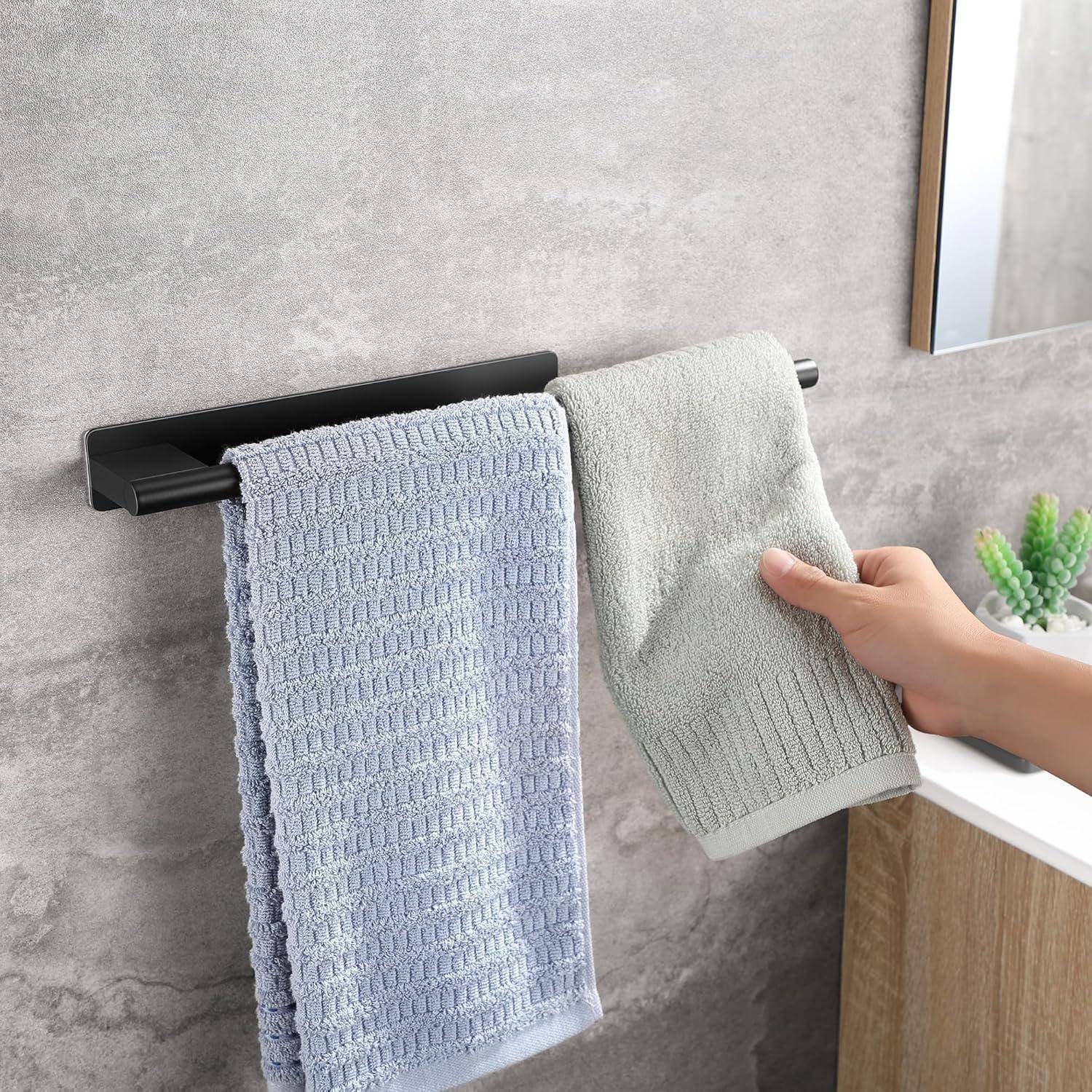 Eine Person hängt ein hellgrünes Handtuch an eine schwarze Handtuchstange neben einem hellblauen Handtuch in einem modernen Badezimmer.