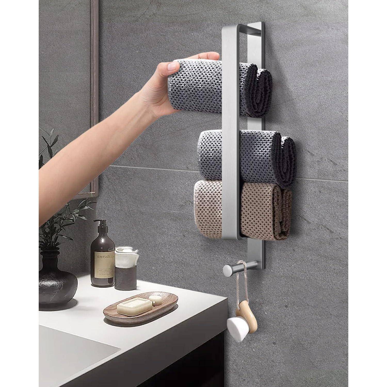Eine Hand legt ein gefaltetes Handtuch auf einen wandmontiertem Handtuchhalter mit vier farbenfrohen Handtüchern. In der Nähe befindet sich eine Arbeitsplatte mit Körperpflegeprodukten und einer Pflanze.