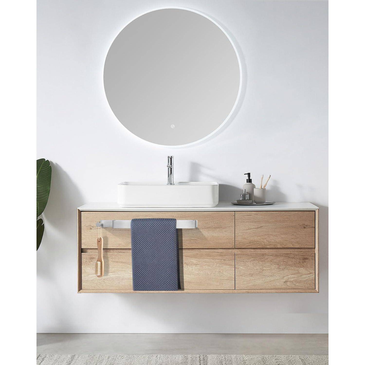 Ein minimalistisches Badezimmer zeigt einen runden Spiegel über einem Holzwaschtisch mit einem weißen Waschbecken, einem Handtuch und einem Seifenspender vor einer weißen Wand.