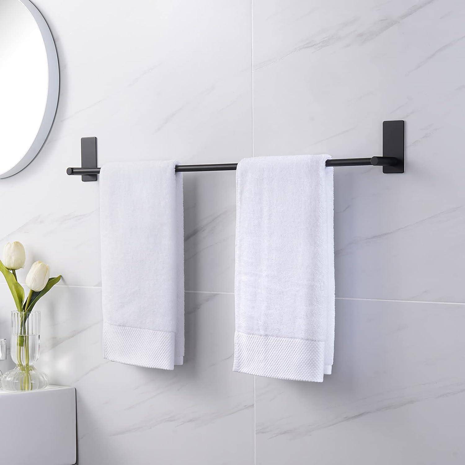 Eine minimalistische Badezimmerszene mit weißen Handtüchern, die an einem schwarzen Handtuchhalter hängen, neben einem runden Spiegel und einer Vase mit weißen Tulpen.