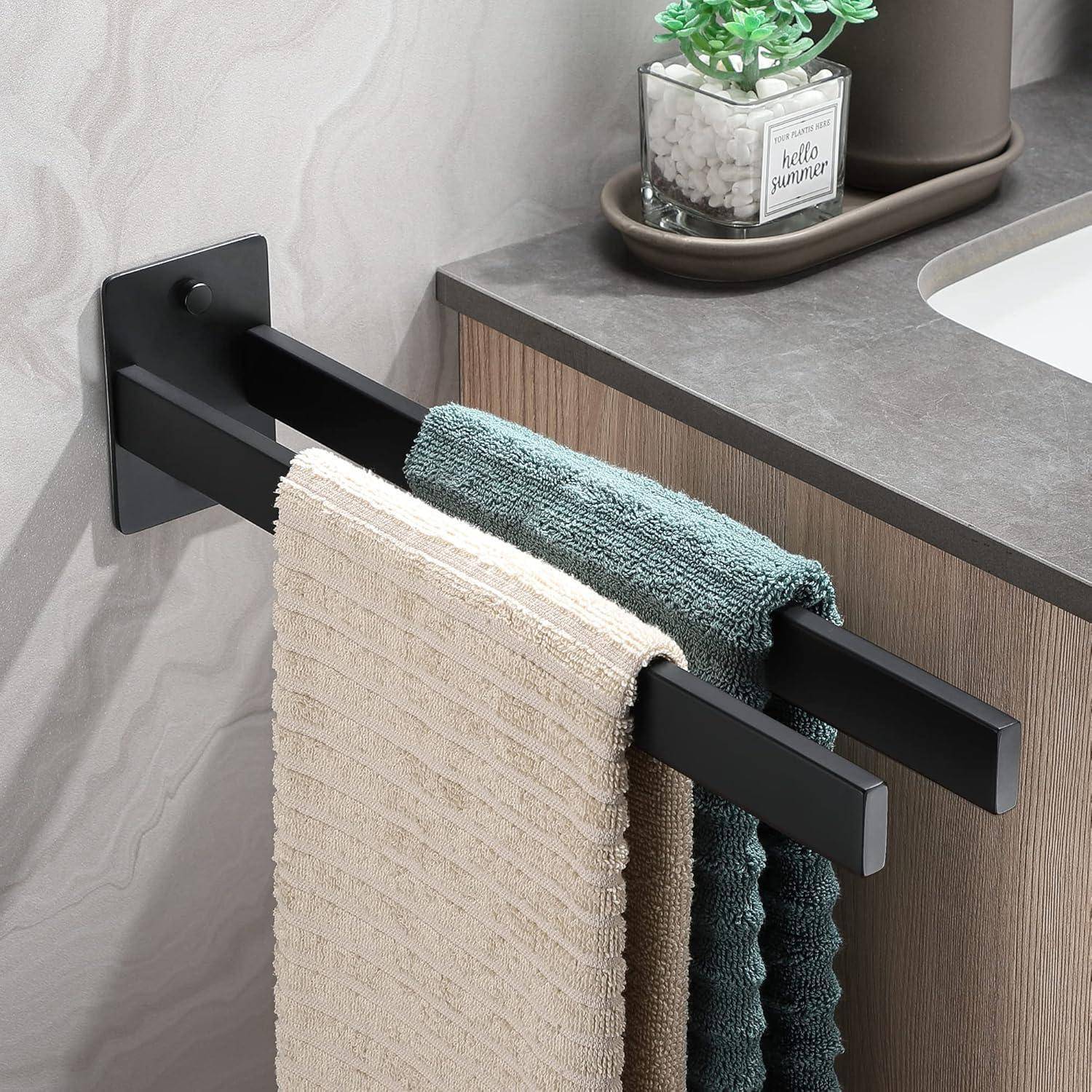 Zwei Handtücher, in den Farben Beige und Petrol, hängen an schwarzen Metallstangen vor einer grauen Wand. Darüber ist eine graue Arbeitsplatte mit einer Topfpflanze zu sehen.