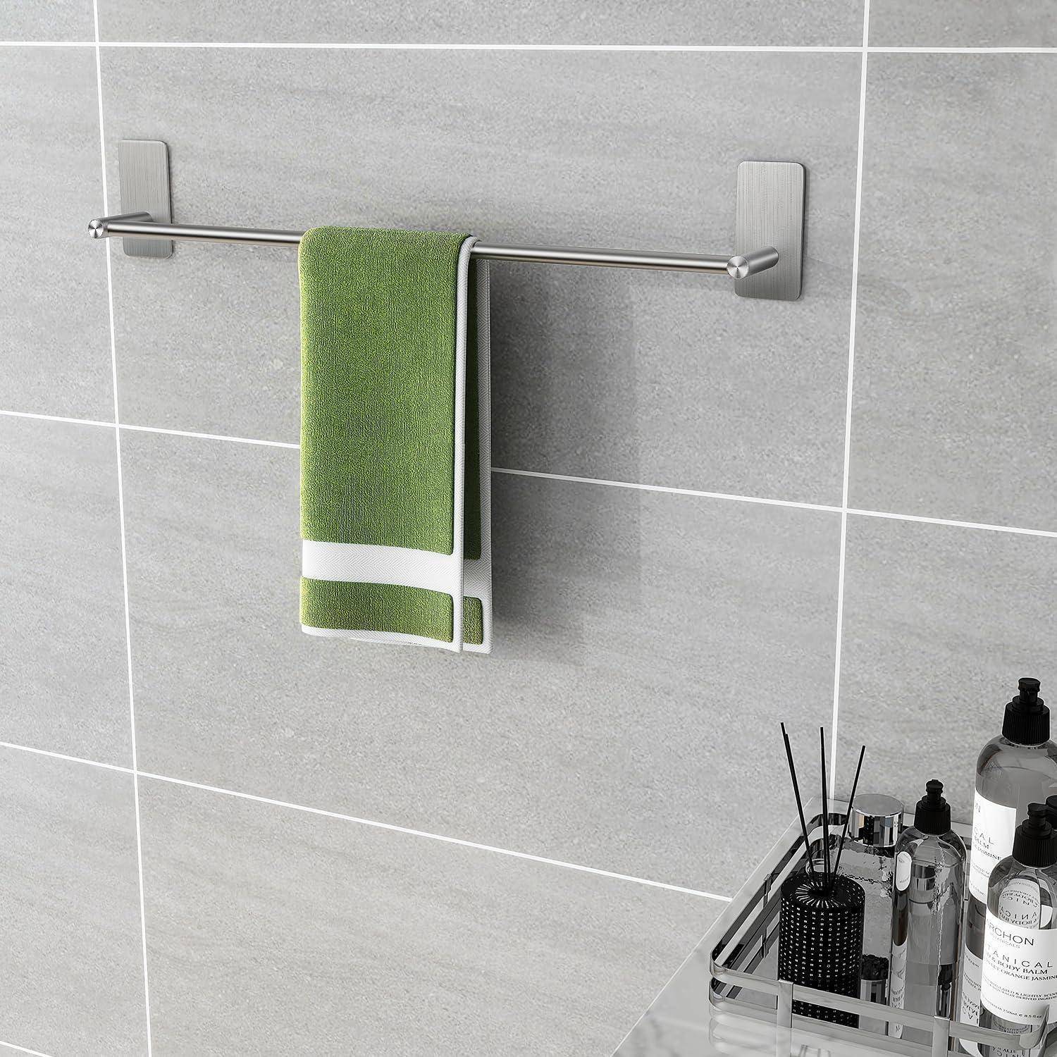 Ein grünes Handtuch mit weißen Streifen hängt an einer Metallhandtuchstange, die an einer grauen Fliesenwand befestigt ist. In der Nähe stehen Toilettenartikel auf einem Glasregal.