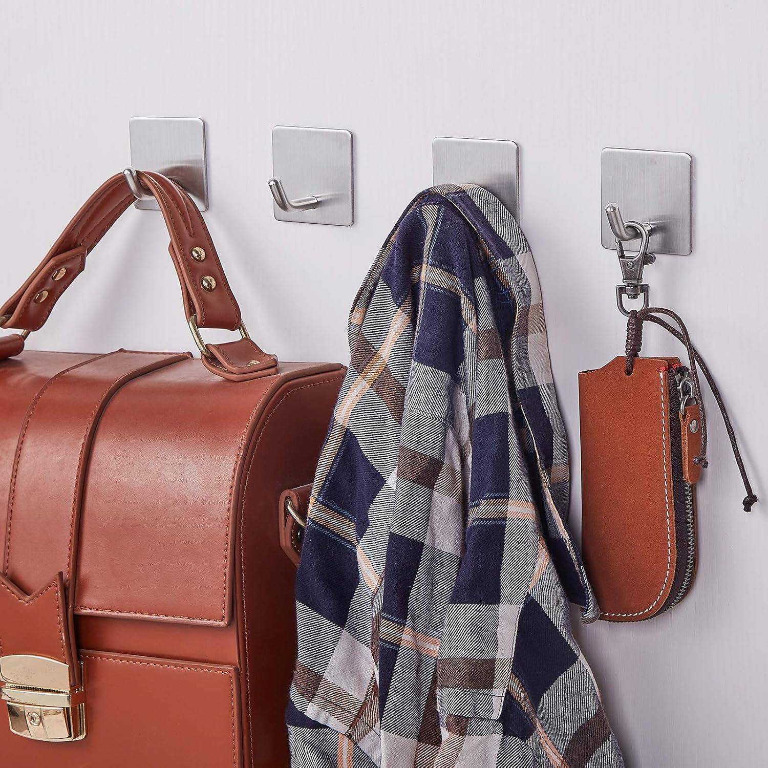 Eine Wand mit vier Haken trägt eine braune Handtasche, einen karierten Schal, einen einzelnen Haken und einen Schlüsselbund mit einem braunen Lederschlüsselanhänger.